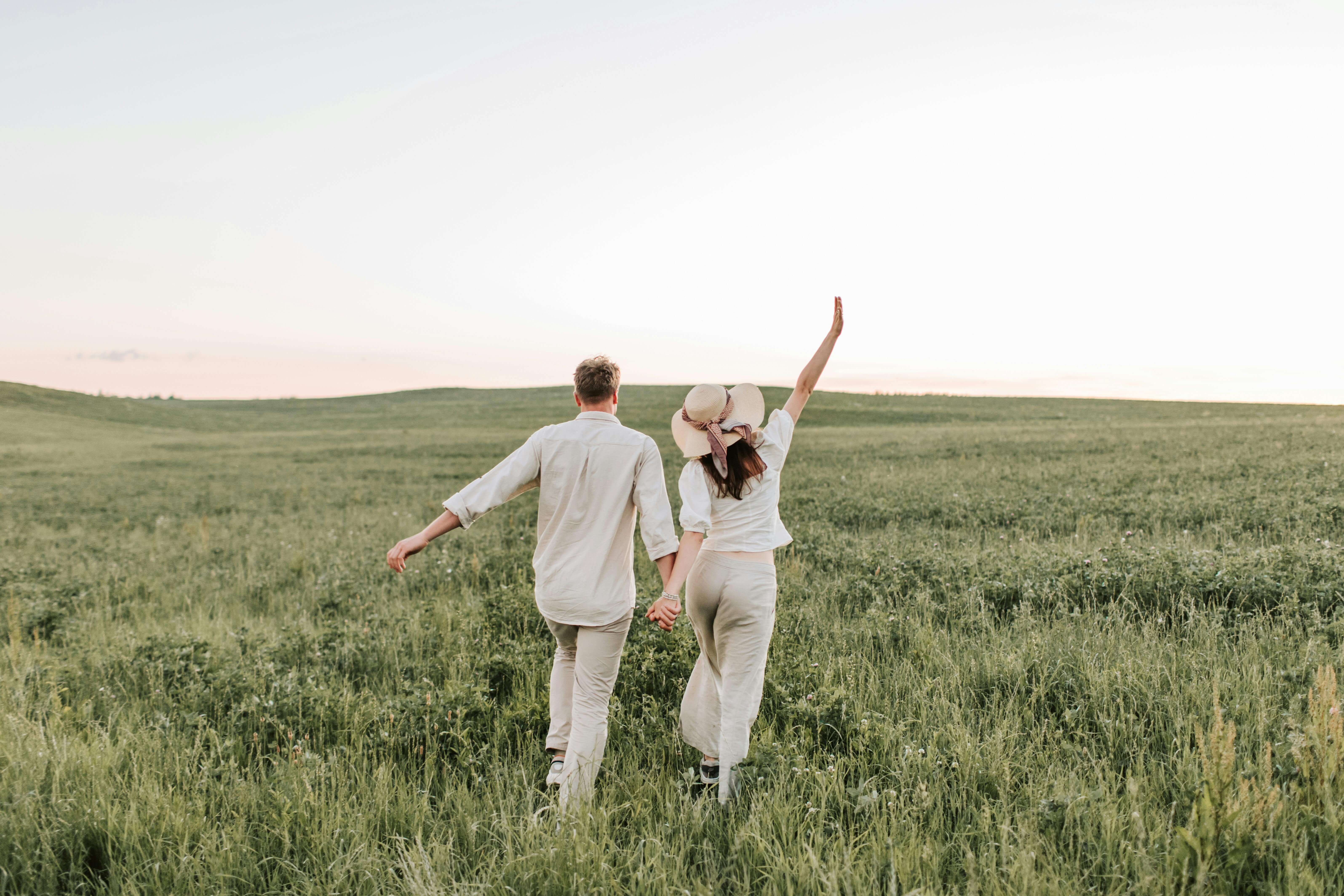 A couple enjoying a romantic walk in a sunlit field, holding hands in nature.