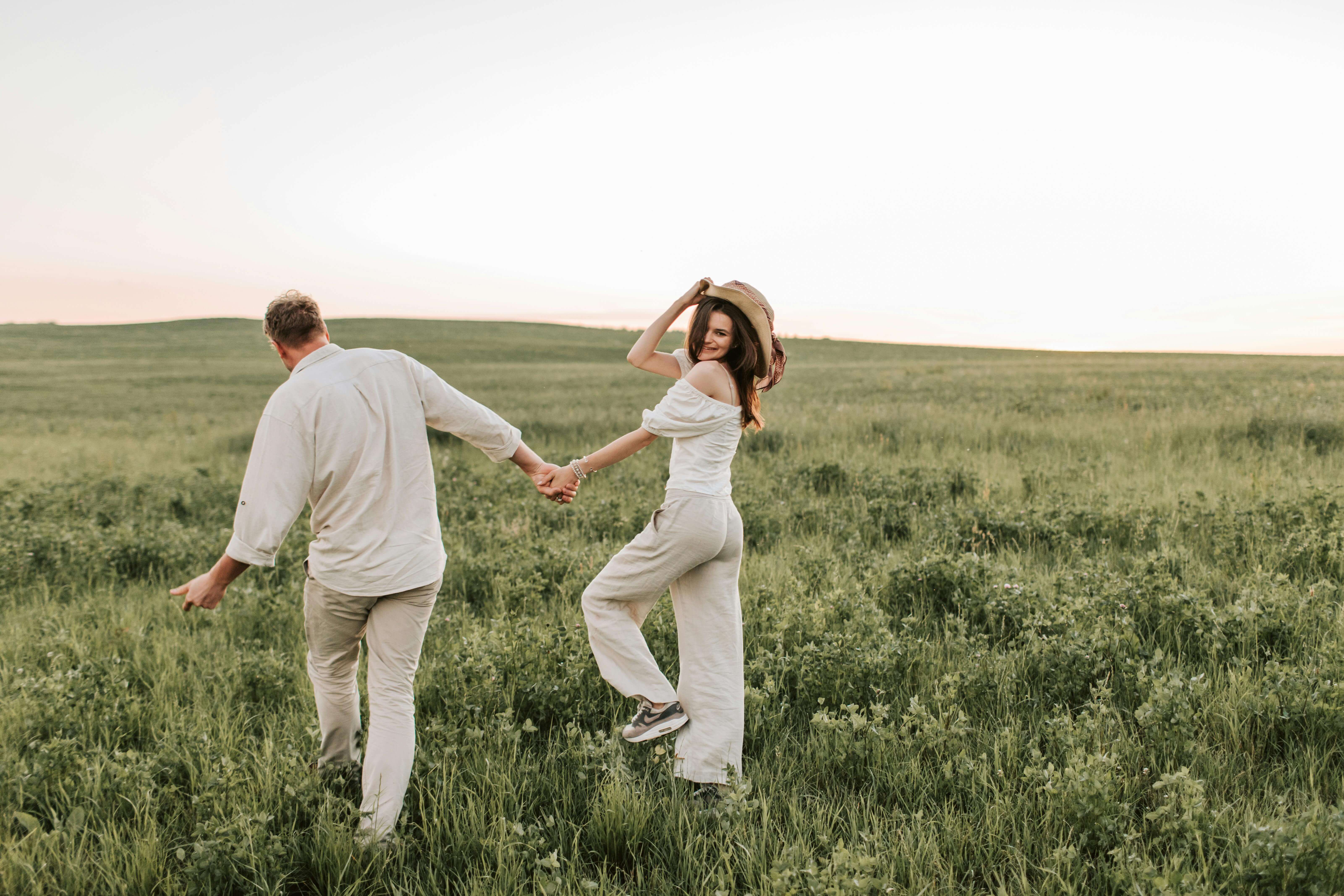A happy couple strolling hand in hand through a green field on a sunny day.