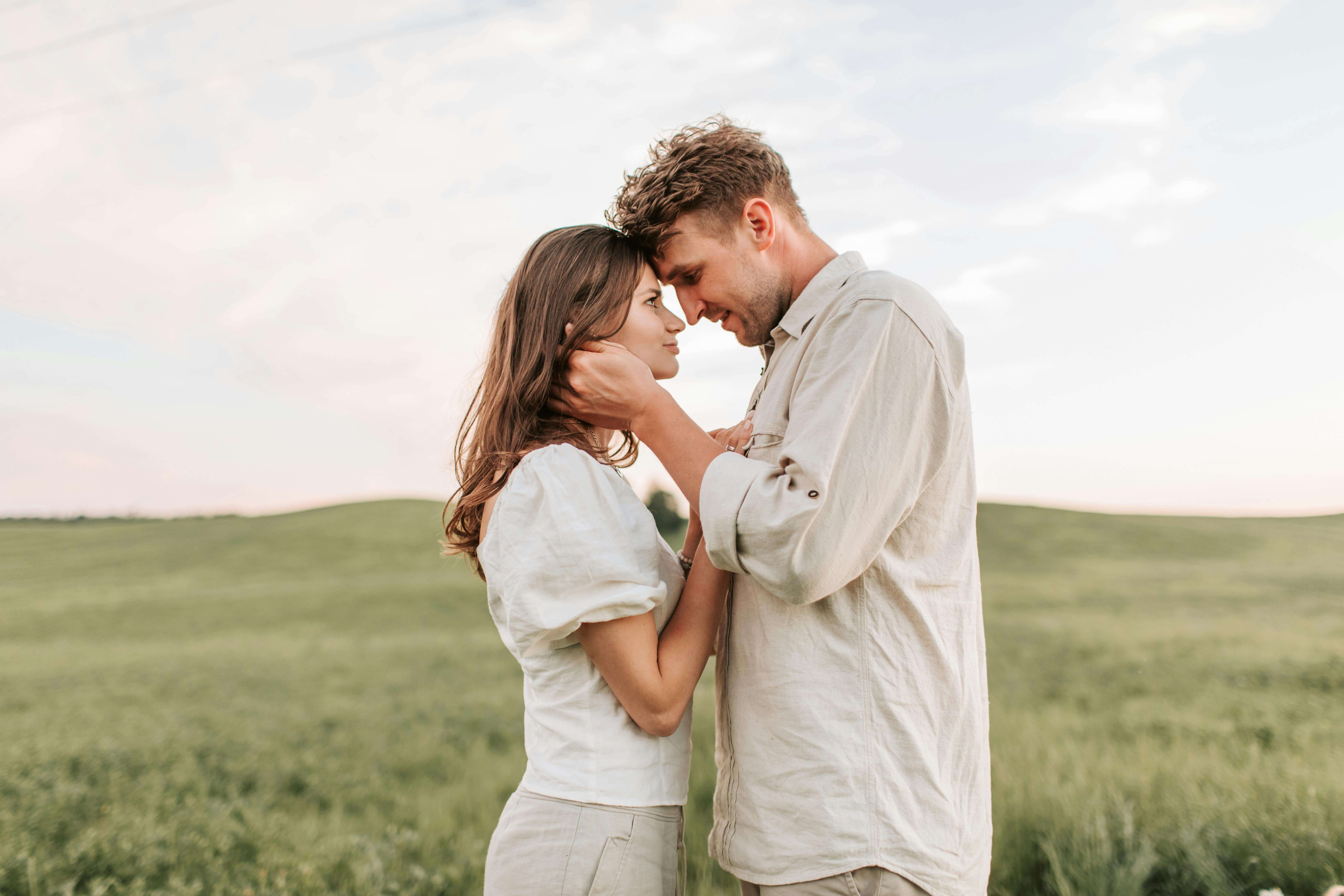 A loving couple embraces in a picturesque field during sunset, capturing a romantic moment.