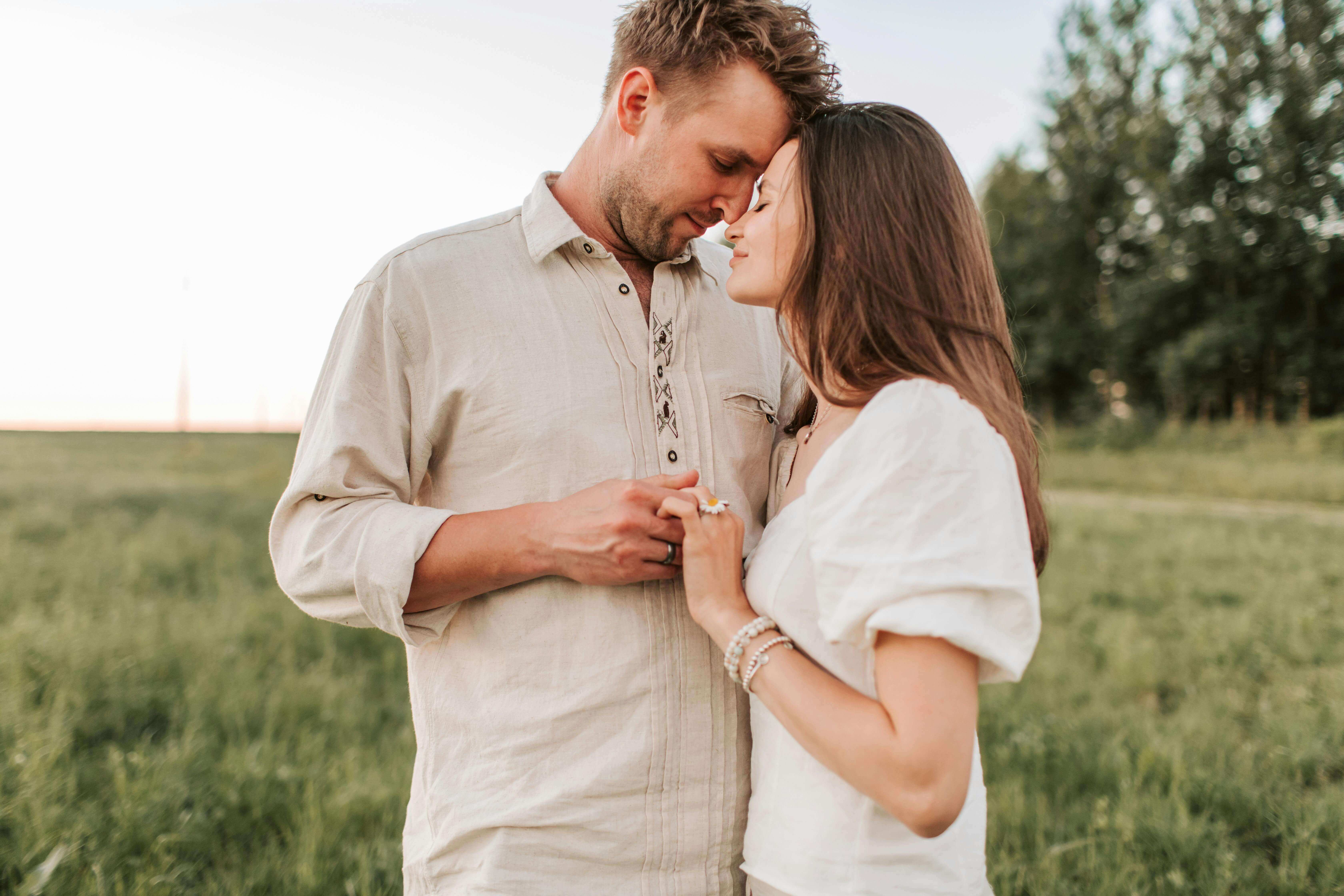 A romantic moment between a couple embracing face to face in a grassy field at sunset.