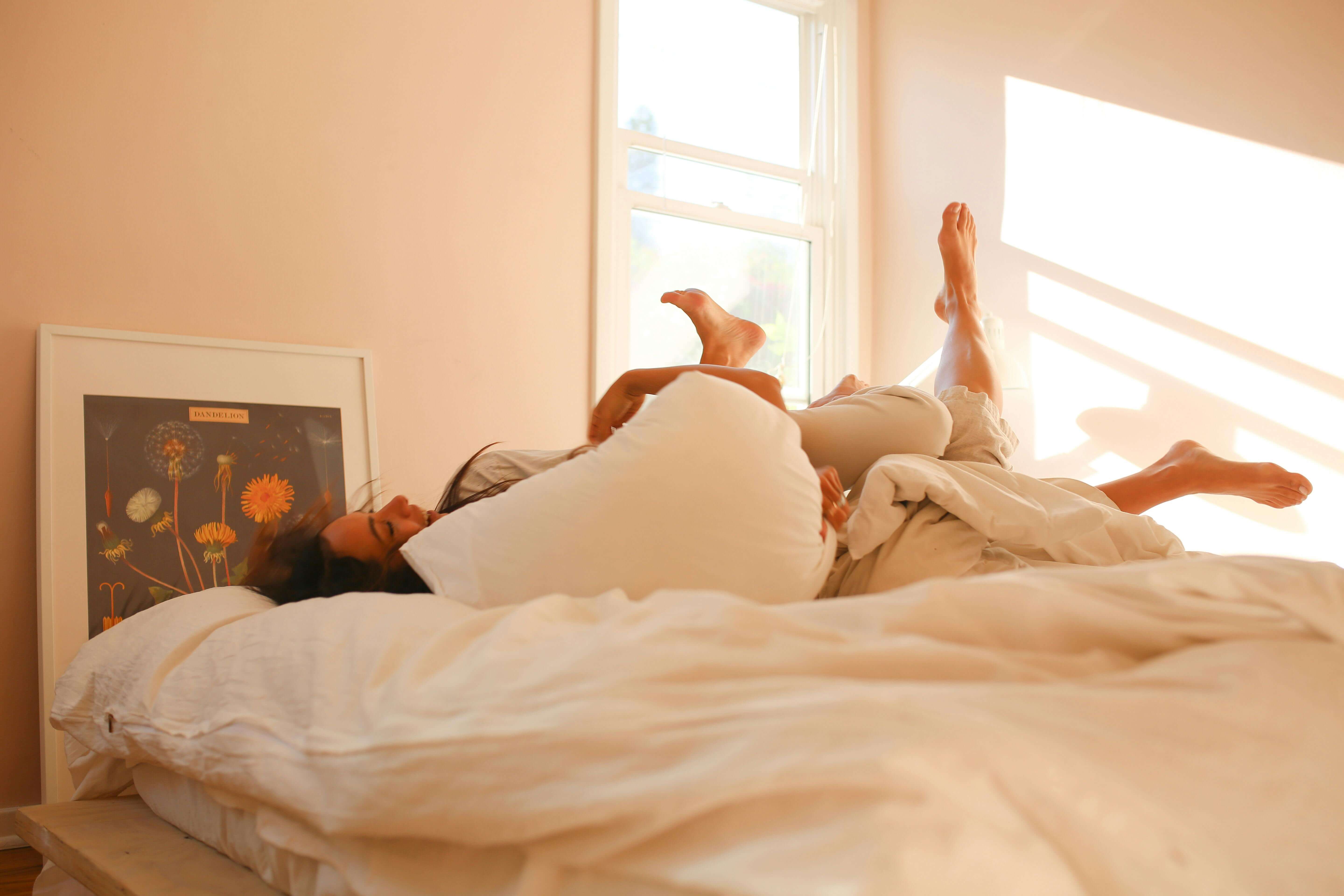 Couple playfully enjoying a relaxed morning on a sunlit bed, capturing a moment of joy and intimacy.