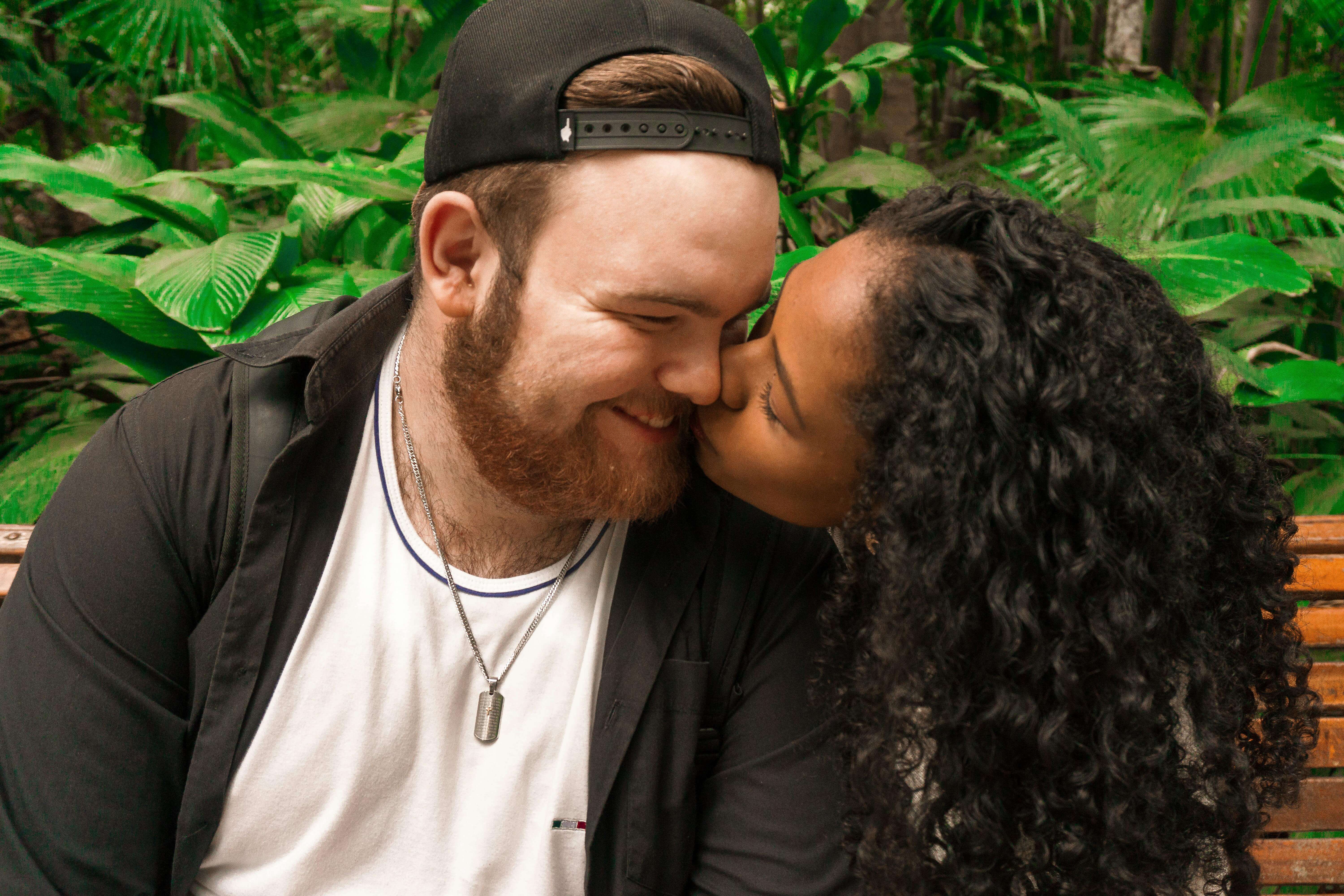 A loving couple kisses tenderly while seated outdoors in lush greenery, showcasing affection and intimacy.