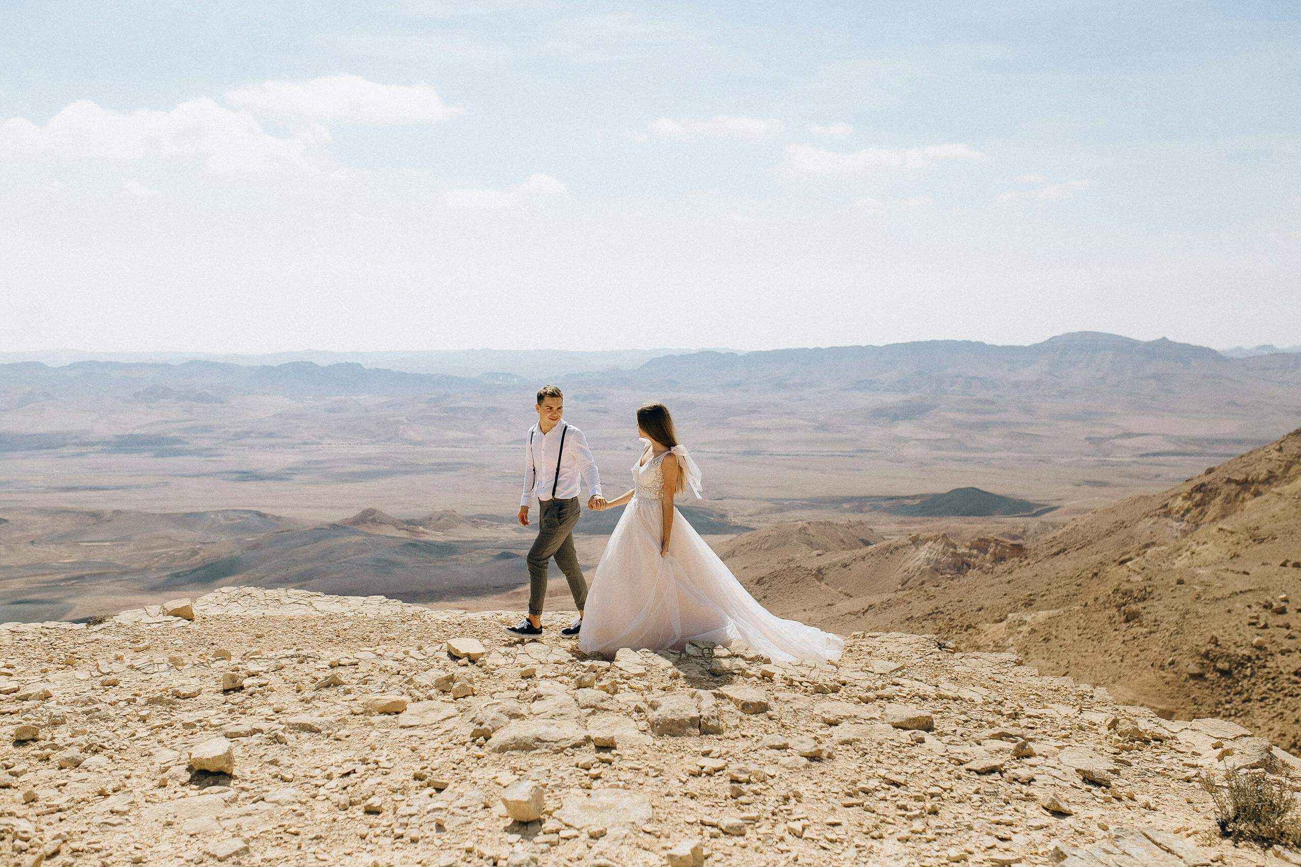 Bride and groom hold hands while walking in a majestic desert scenery.