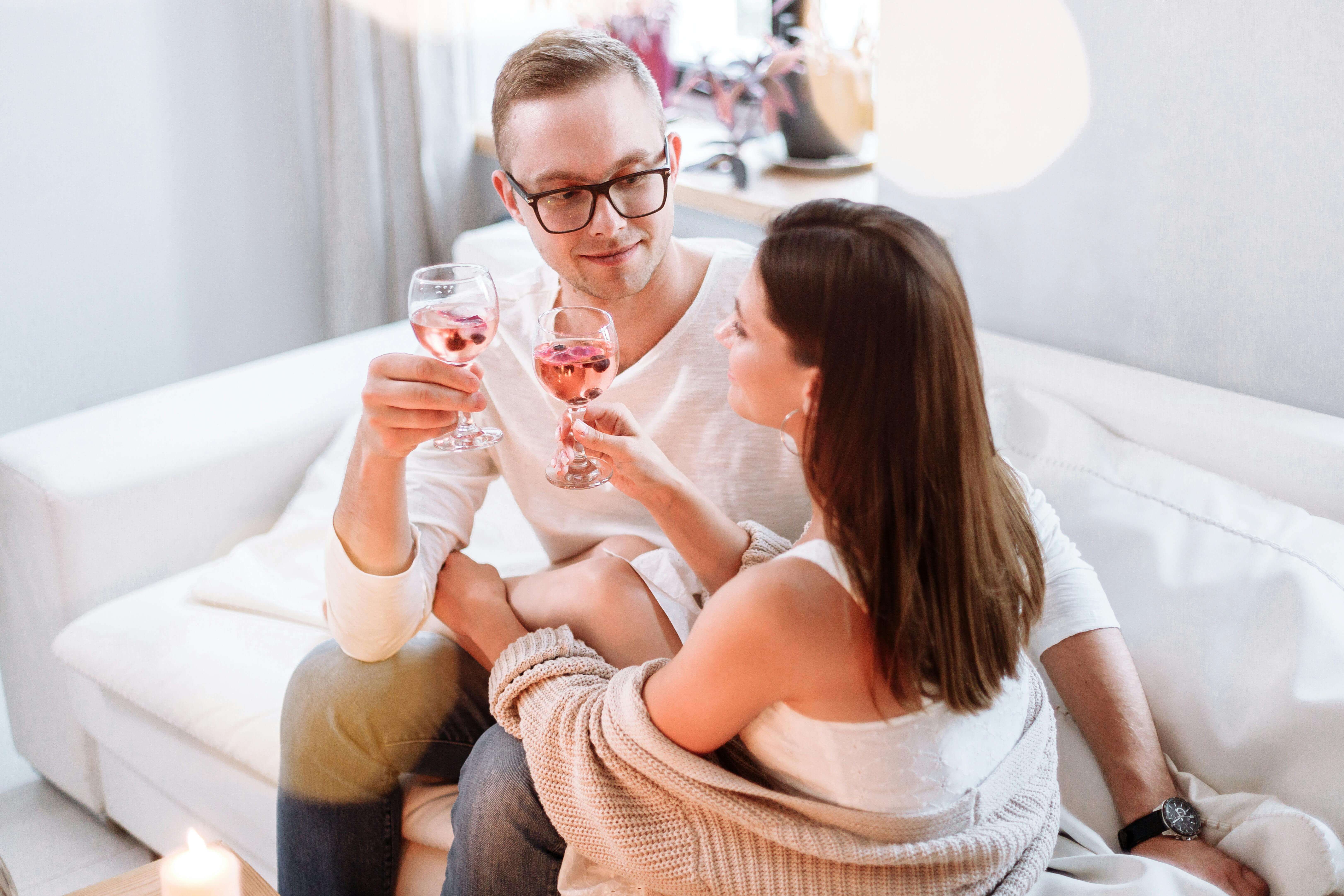A happy couple sitting on a sofa, enjoying wine and each other's company in a cozy indoor setting.