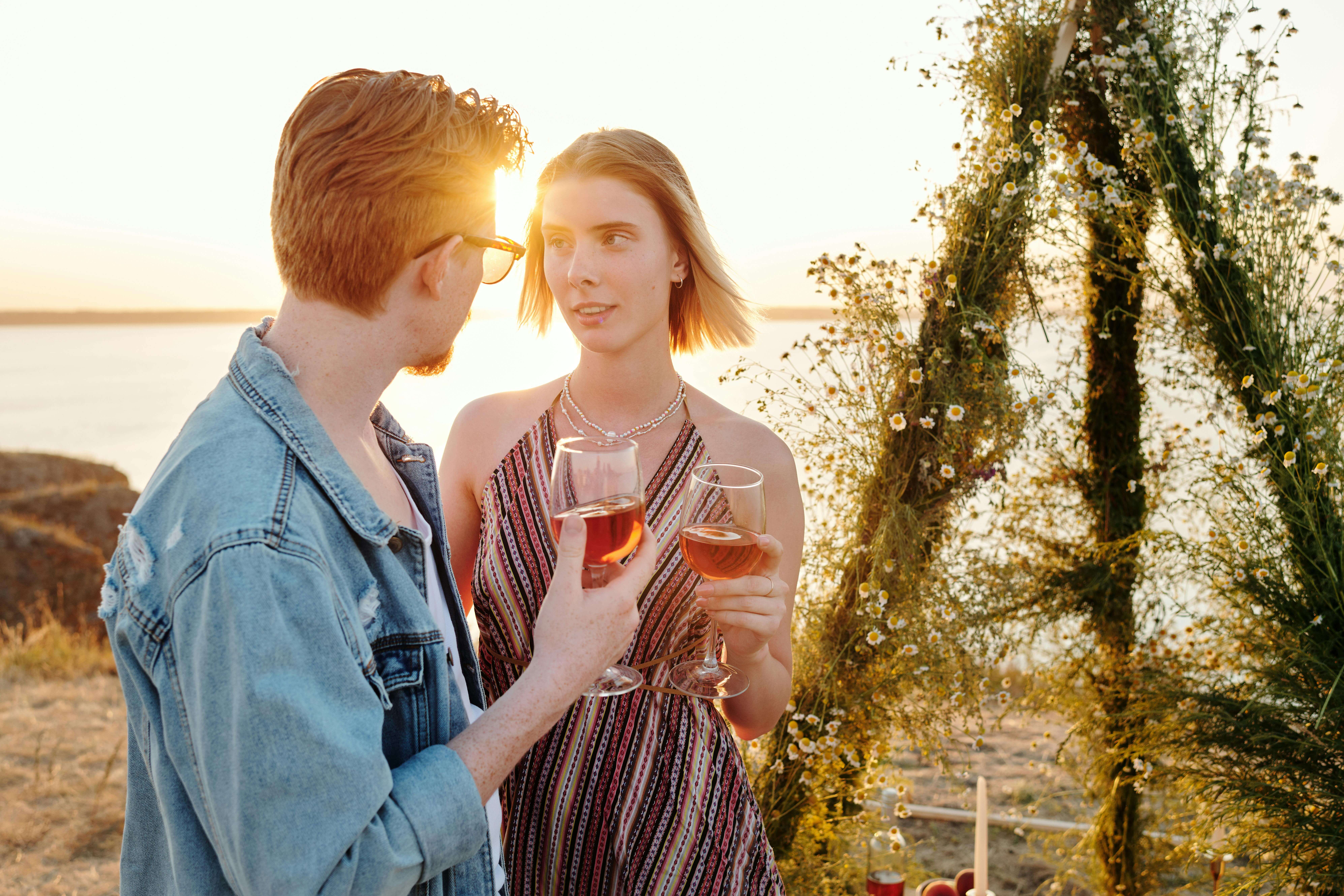A couple enjoying wine during a romantic sunset outdoors by the water.