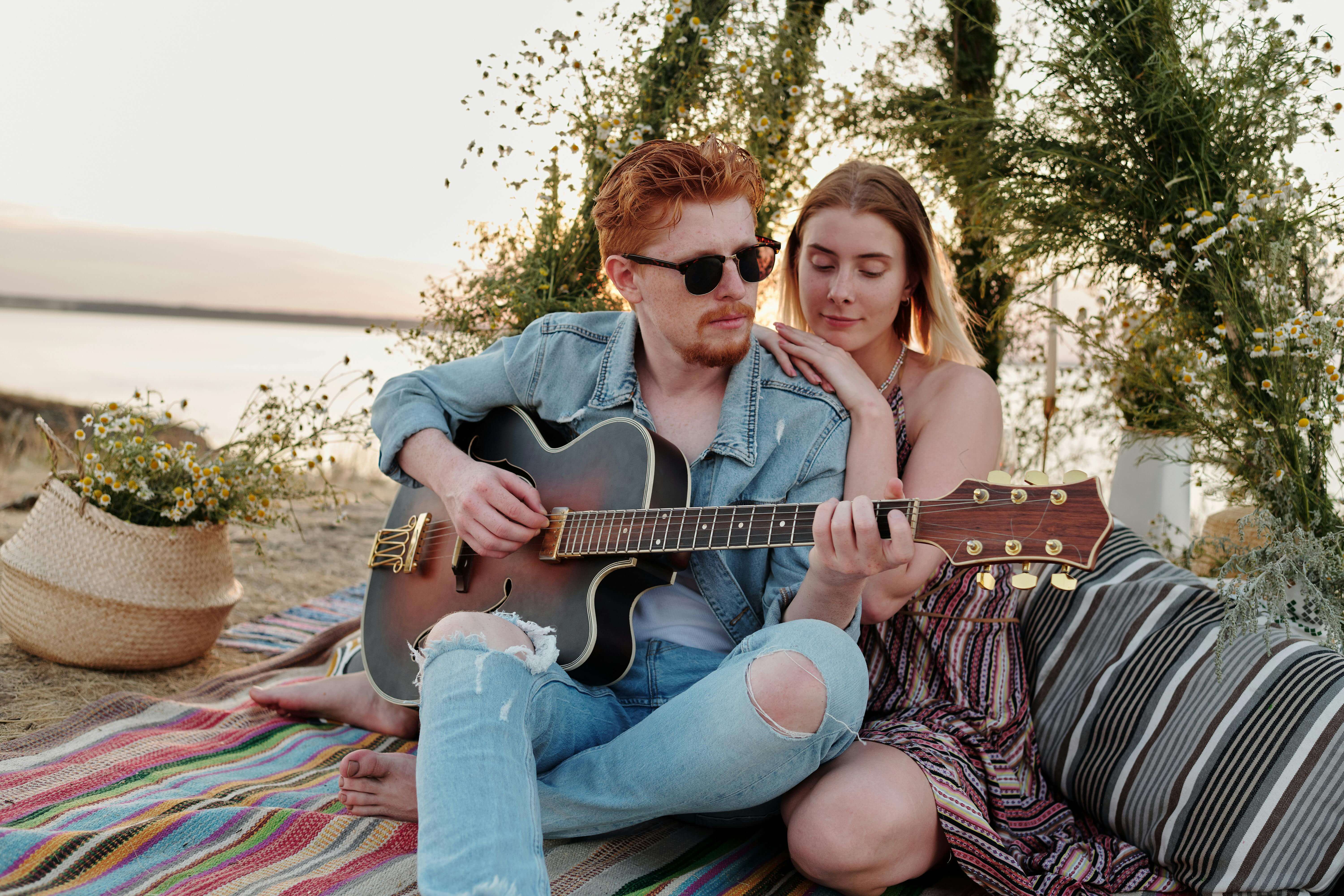 Couple enjoying a romantic moment with a guitar by the lake at sunset.