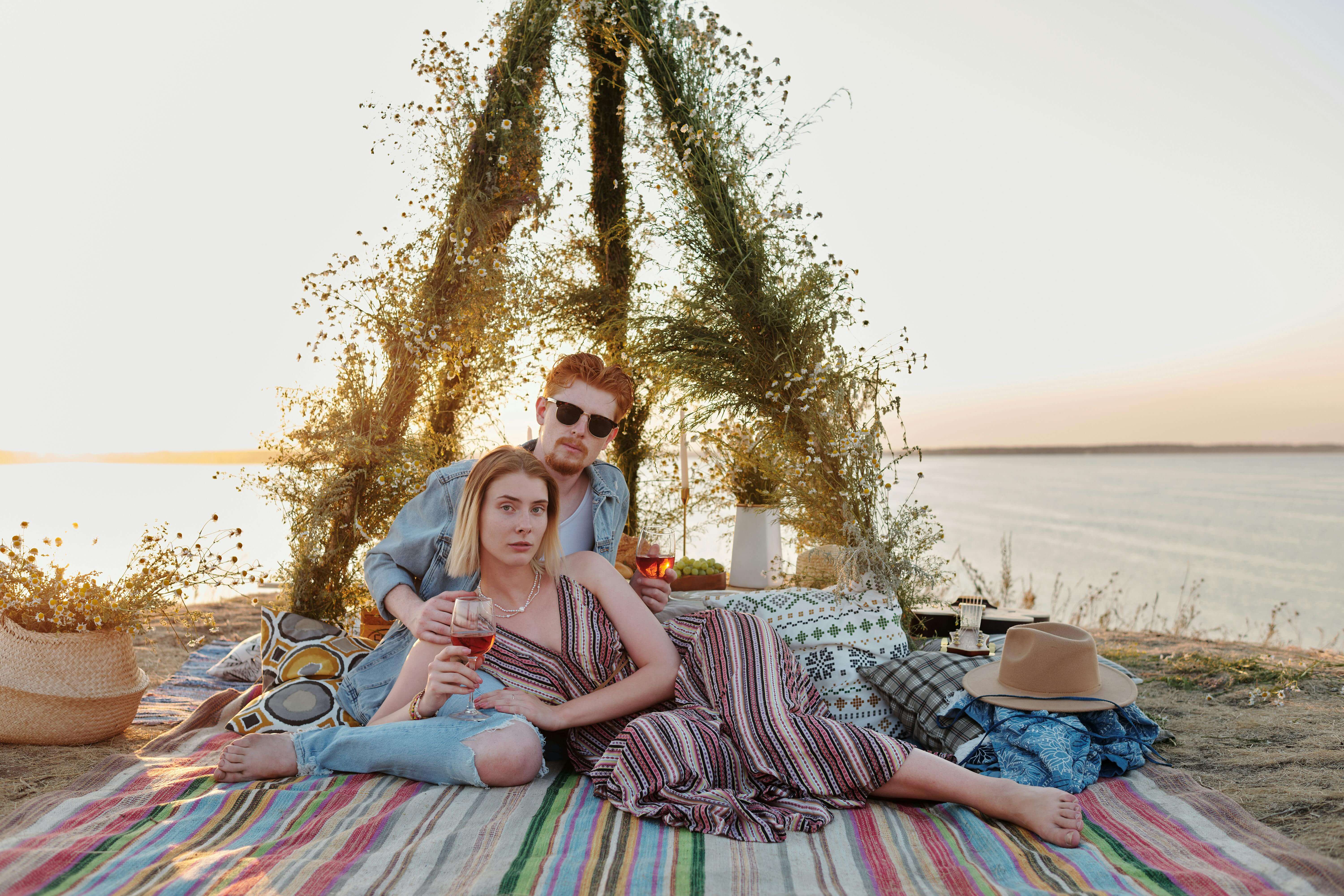 A couple enjoying a romantic picnic on the beach at sunset with wine and a scenic view.