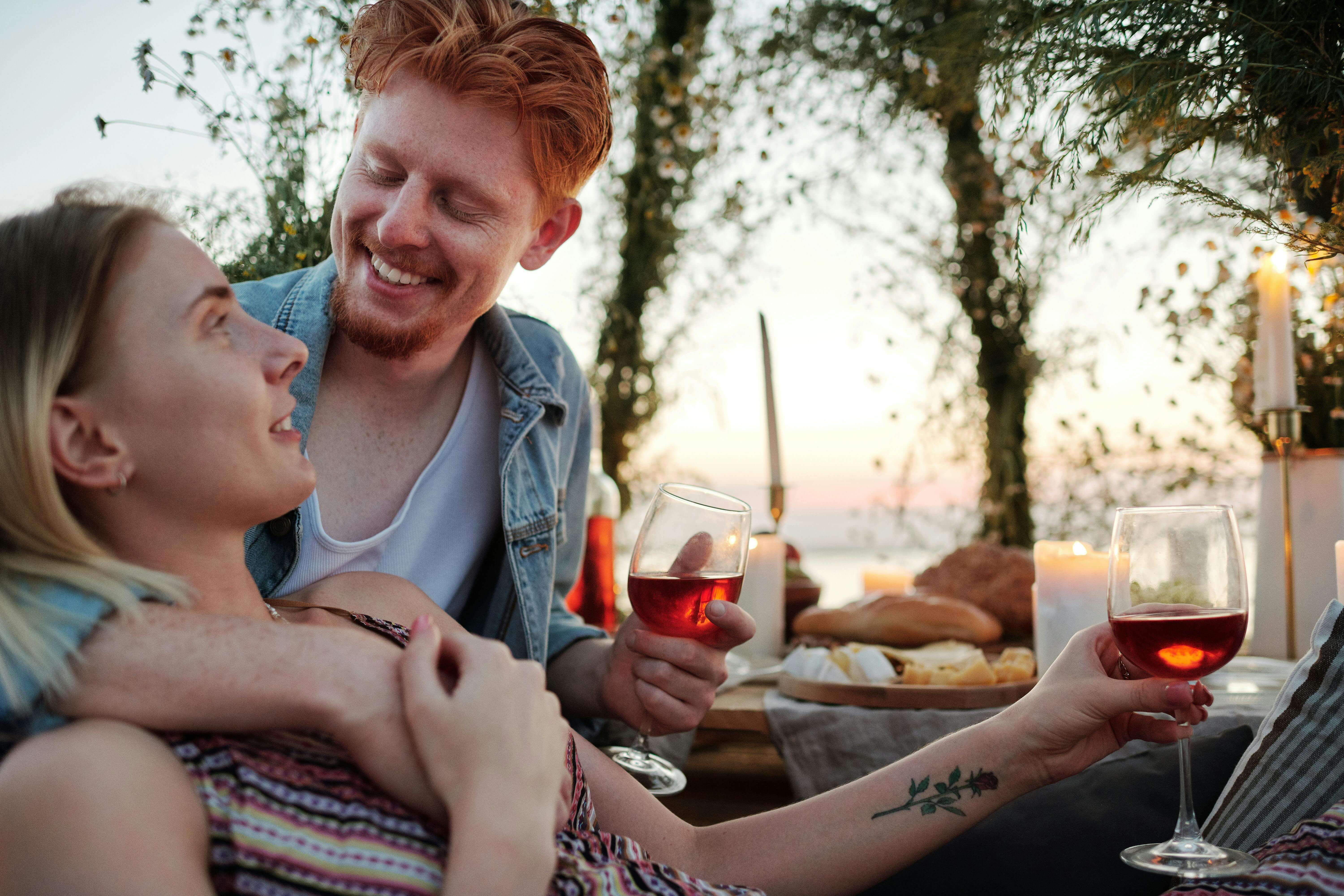 A loving couple shares a joyful moment over wine and dinner at sunset outdoors.