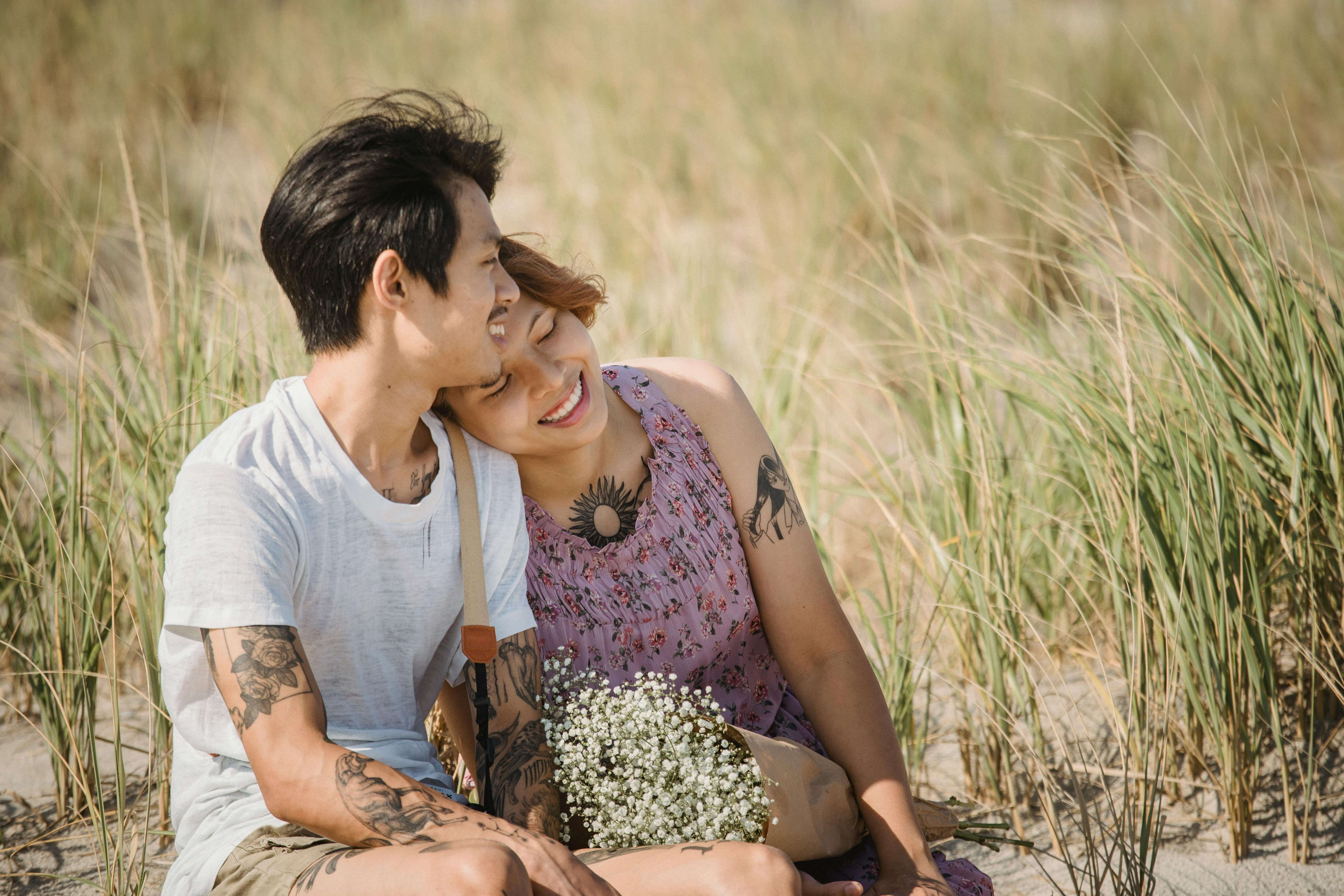 Happy couple sitting together in a sandy grass field, embracing love and nature.