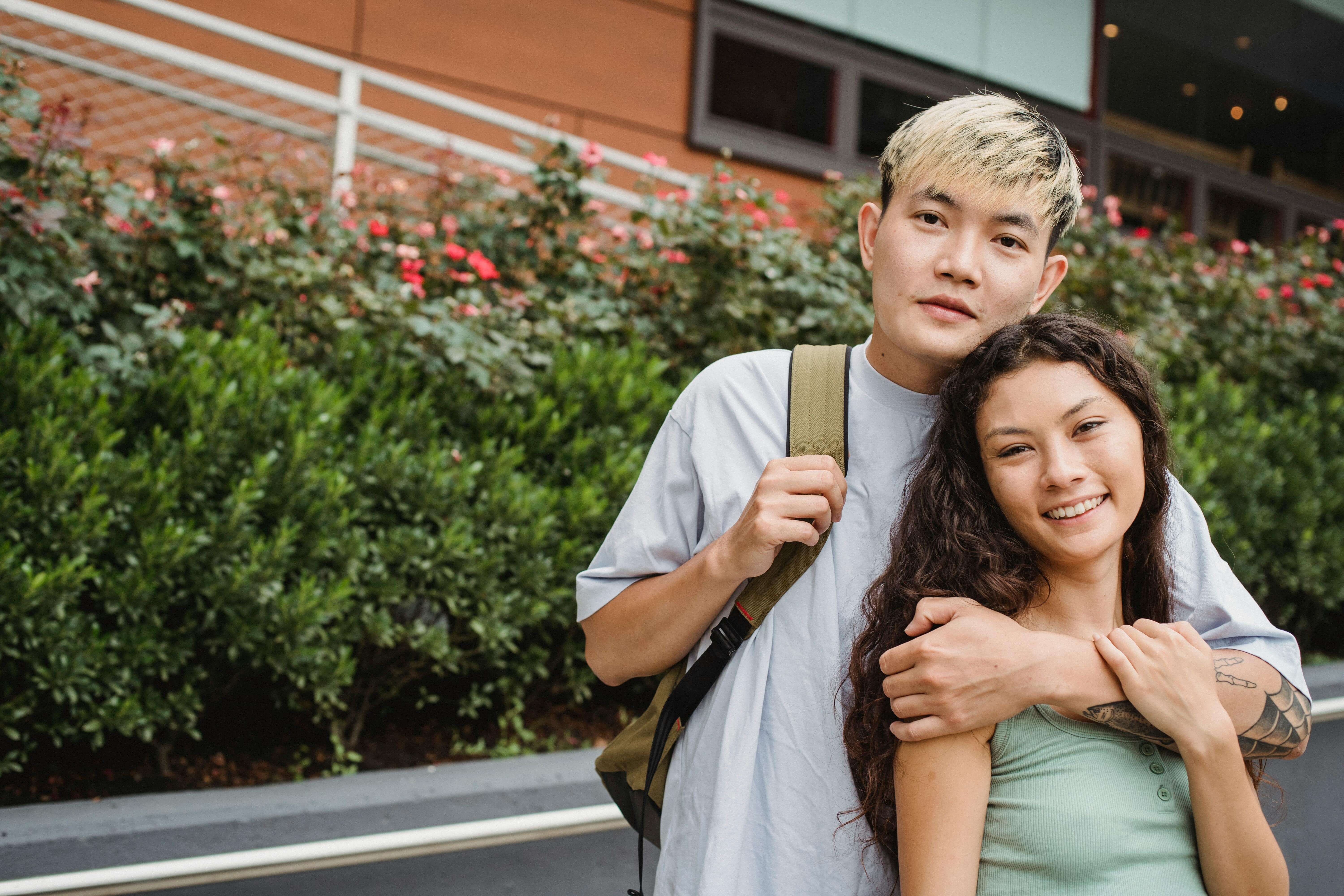 A cheerful couple embracing outdoors, surrounded by greenery and flowers during the day.