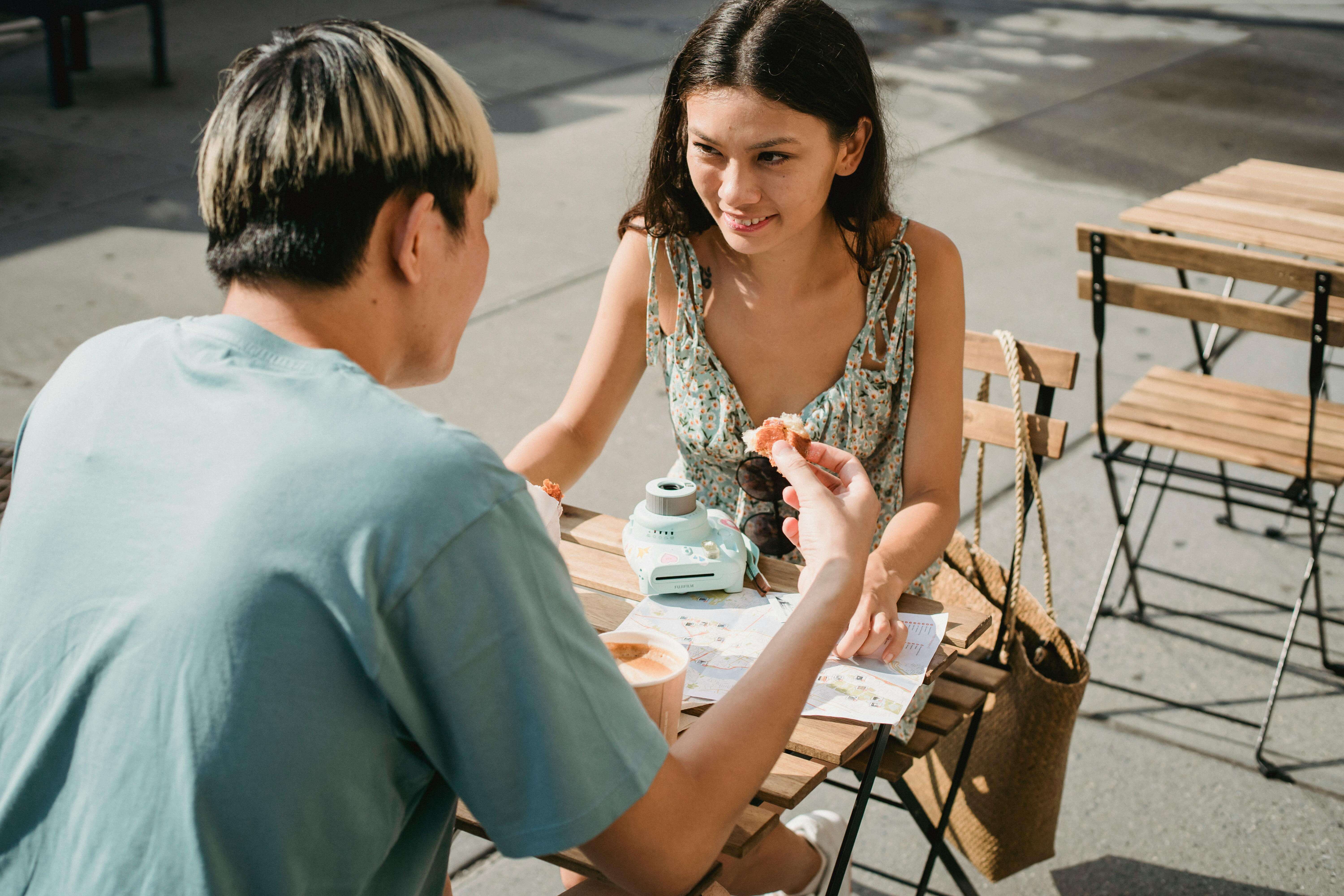 Happy couple enjoying a sunny day at an outdoor cafe, sharing coffee and pastries.
