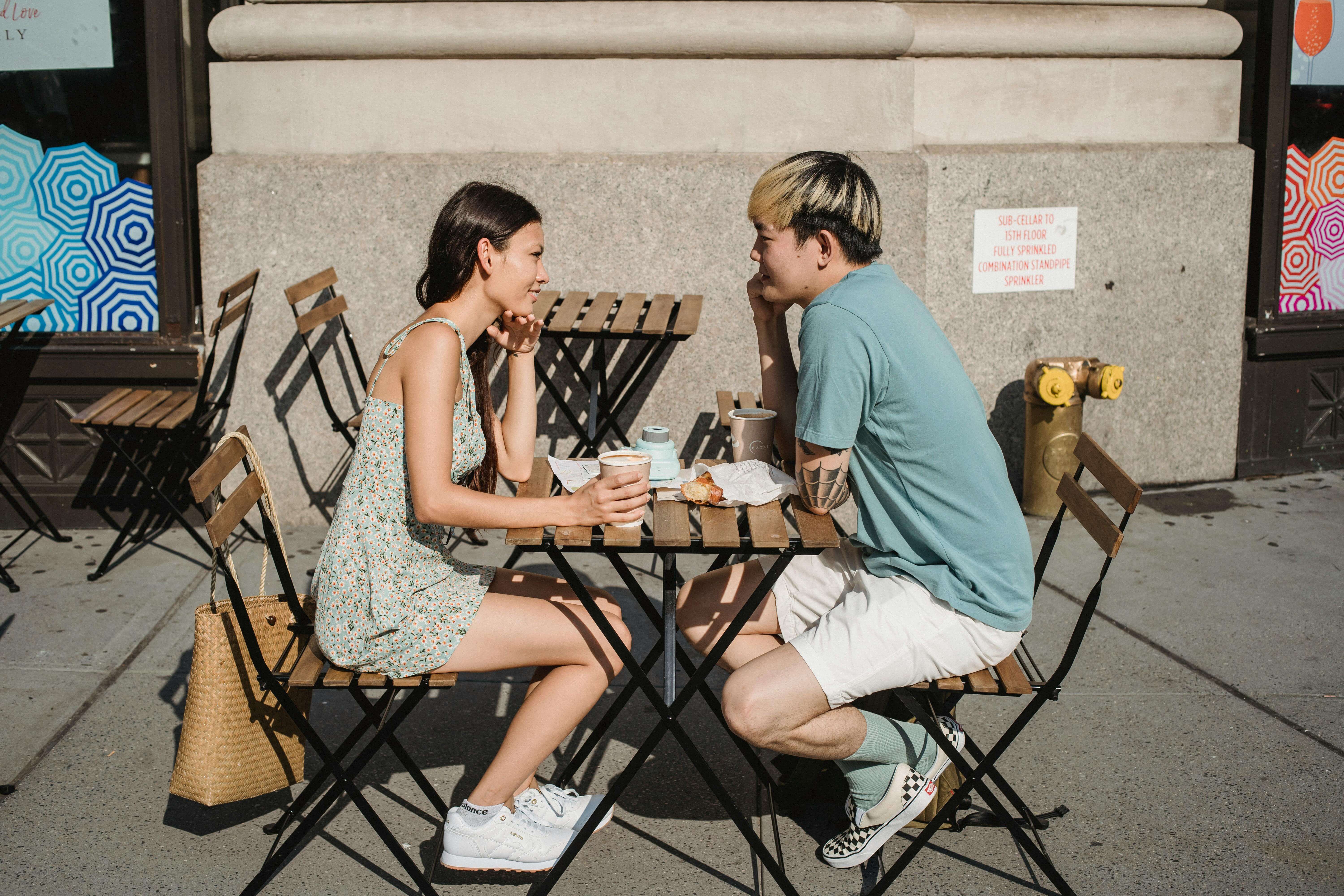 Young couple enjoying a sunny morning coffee date outdoors, smiling and talking.