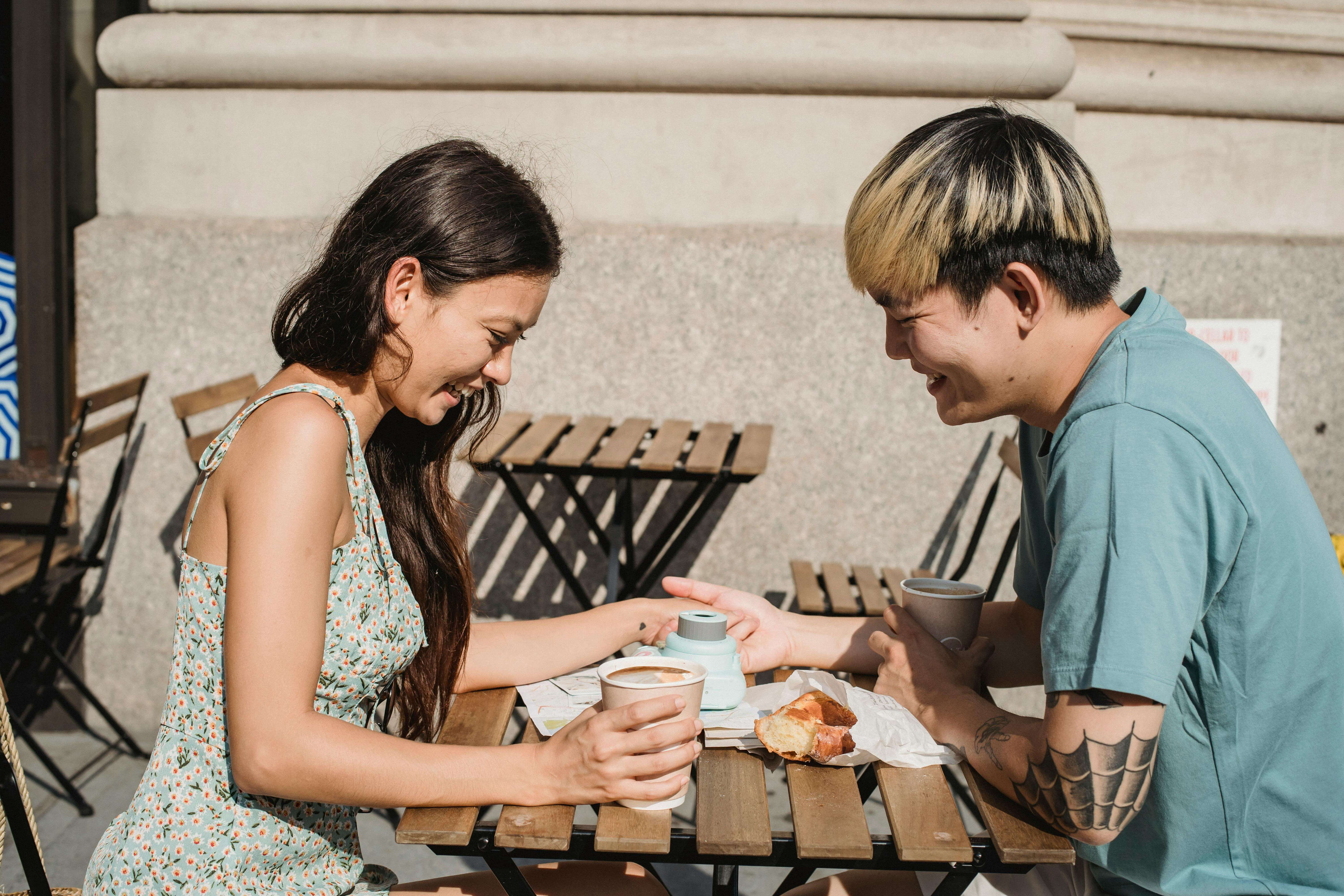 Happy couple having coffee outdoors in a sunny urban setting, sharing a joyful moment together.