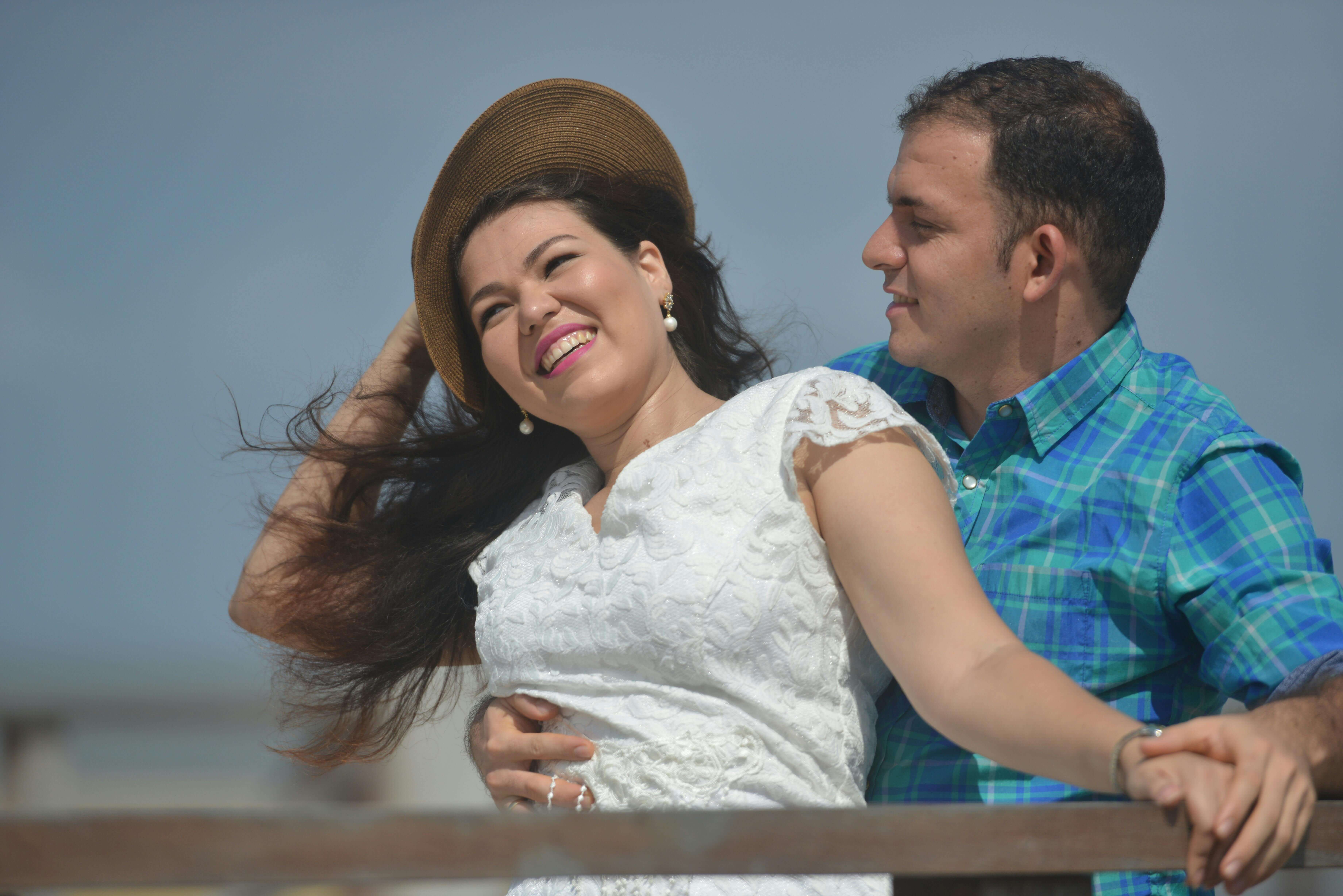 A couple enjoys a windy day, laughing and embracing each other outdoors.