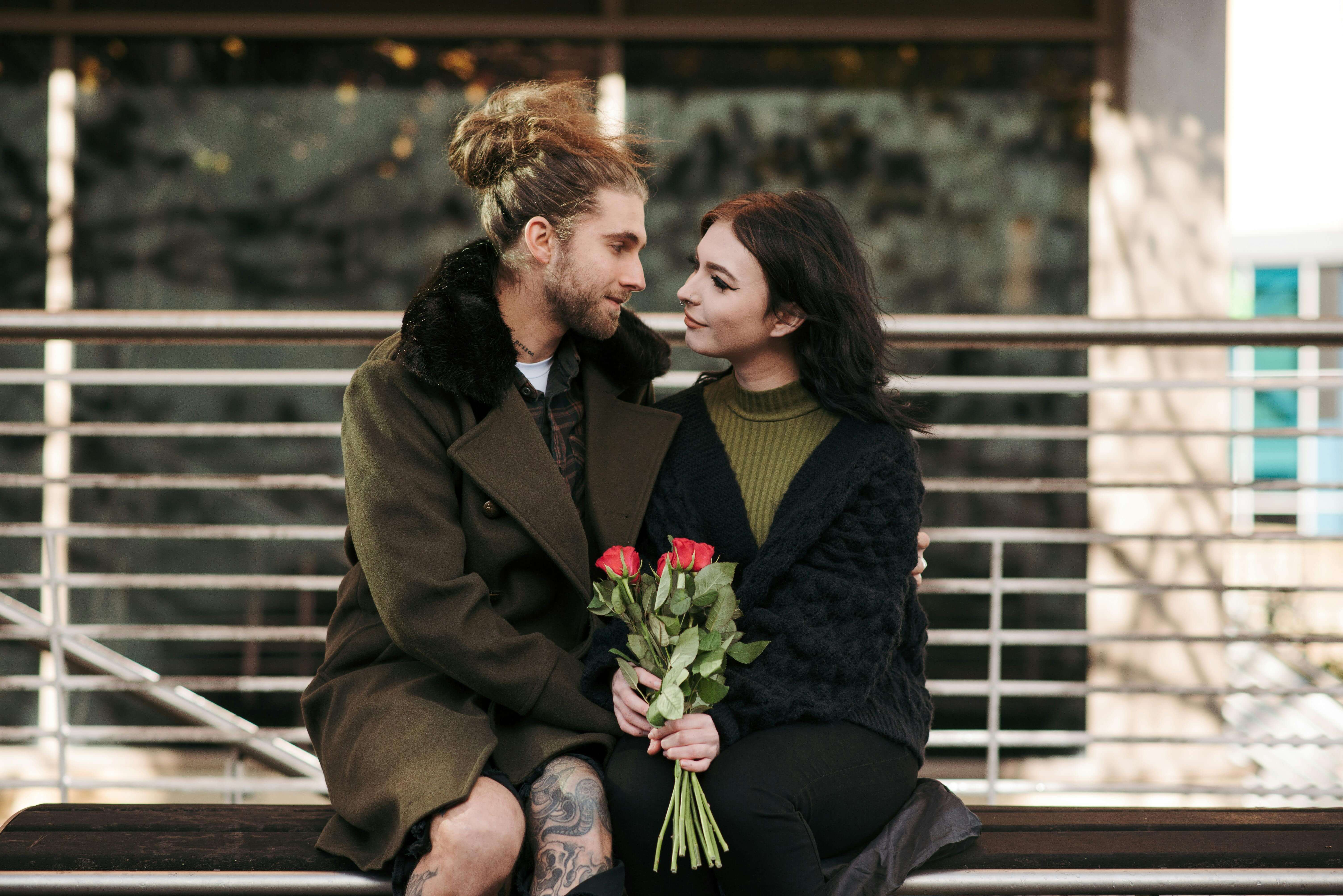 Young couple sitting closely on a bench holding roses, sharing a tender moment.
