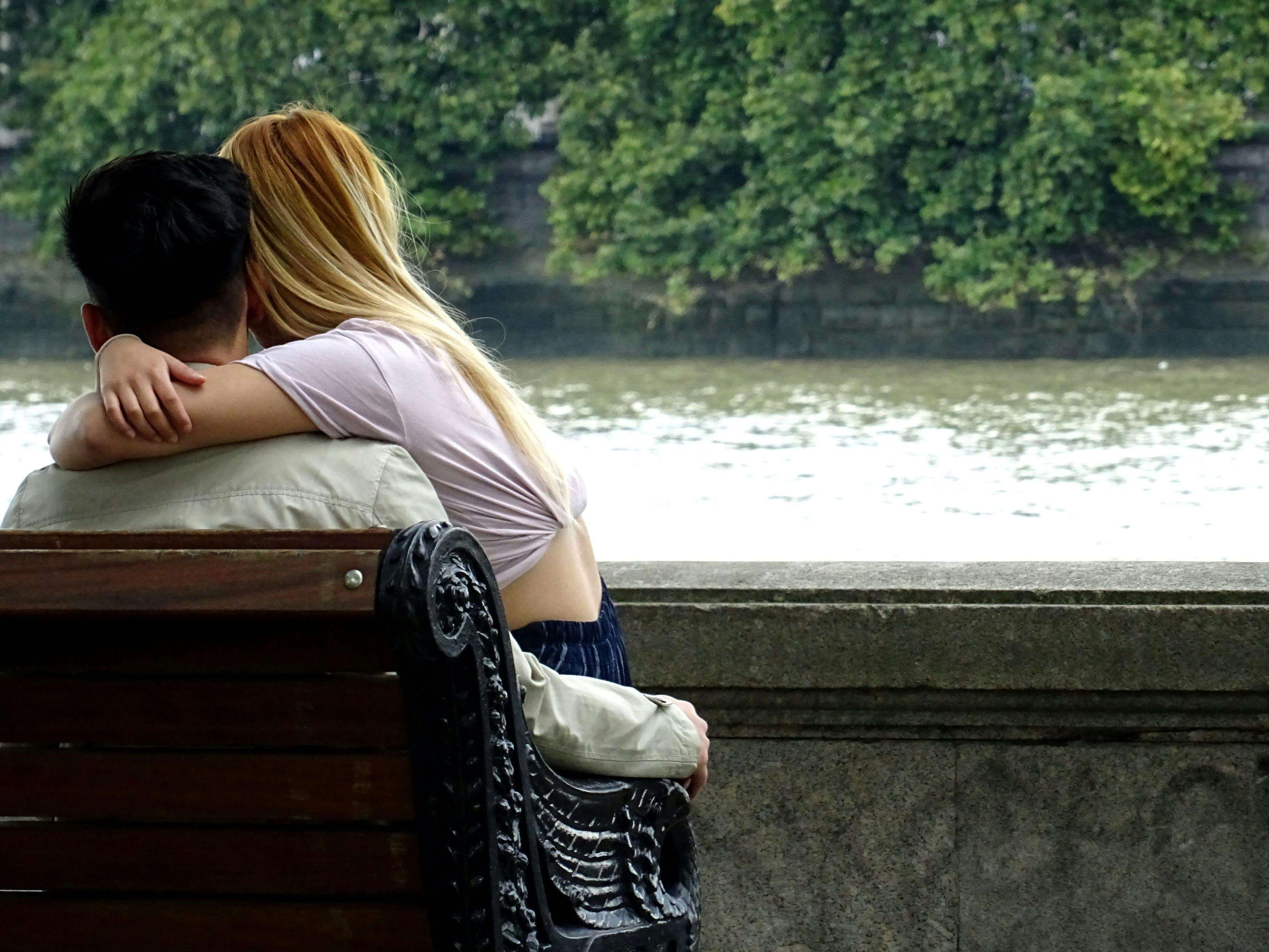 Young couple sharing a tender moment on a park bench by the riverside