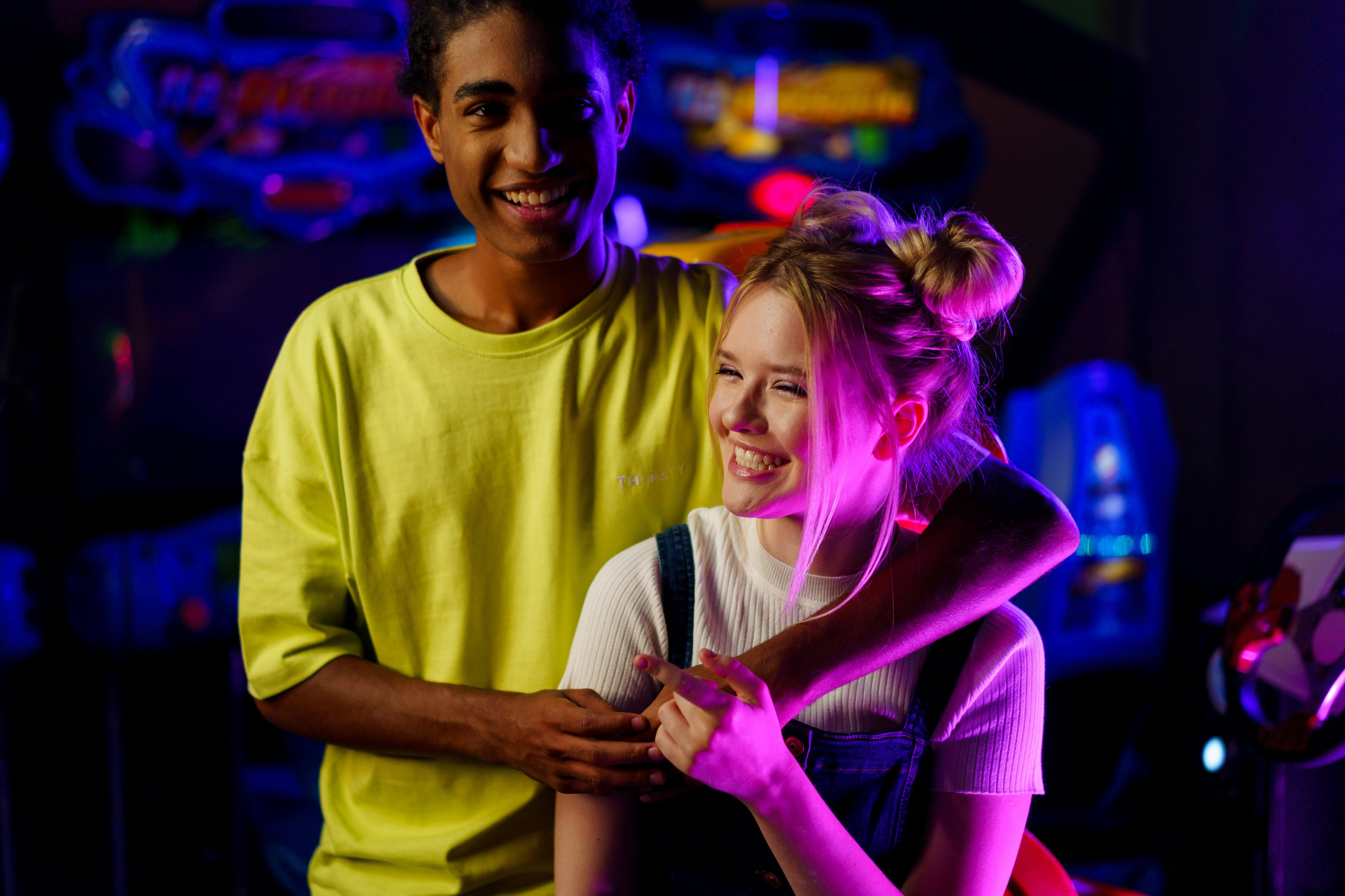 Smiling couple bonding at a vibrant arcade with gaming machines.