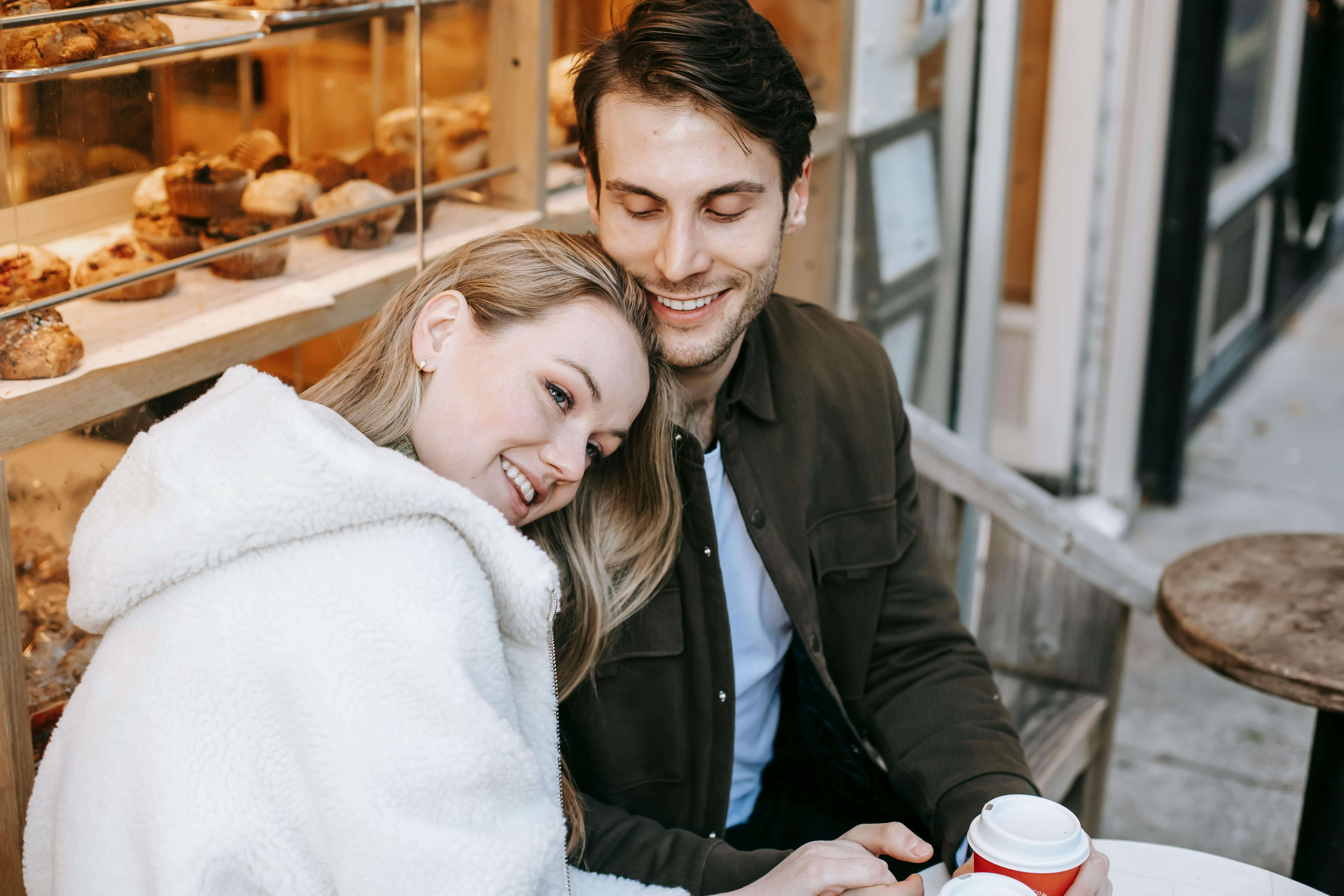 A loving couple shares a warm moment over coffee in a cozy bakery setting.