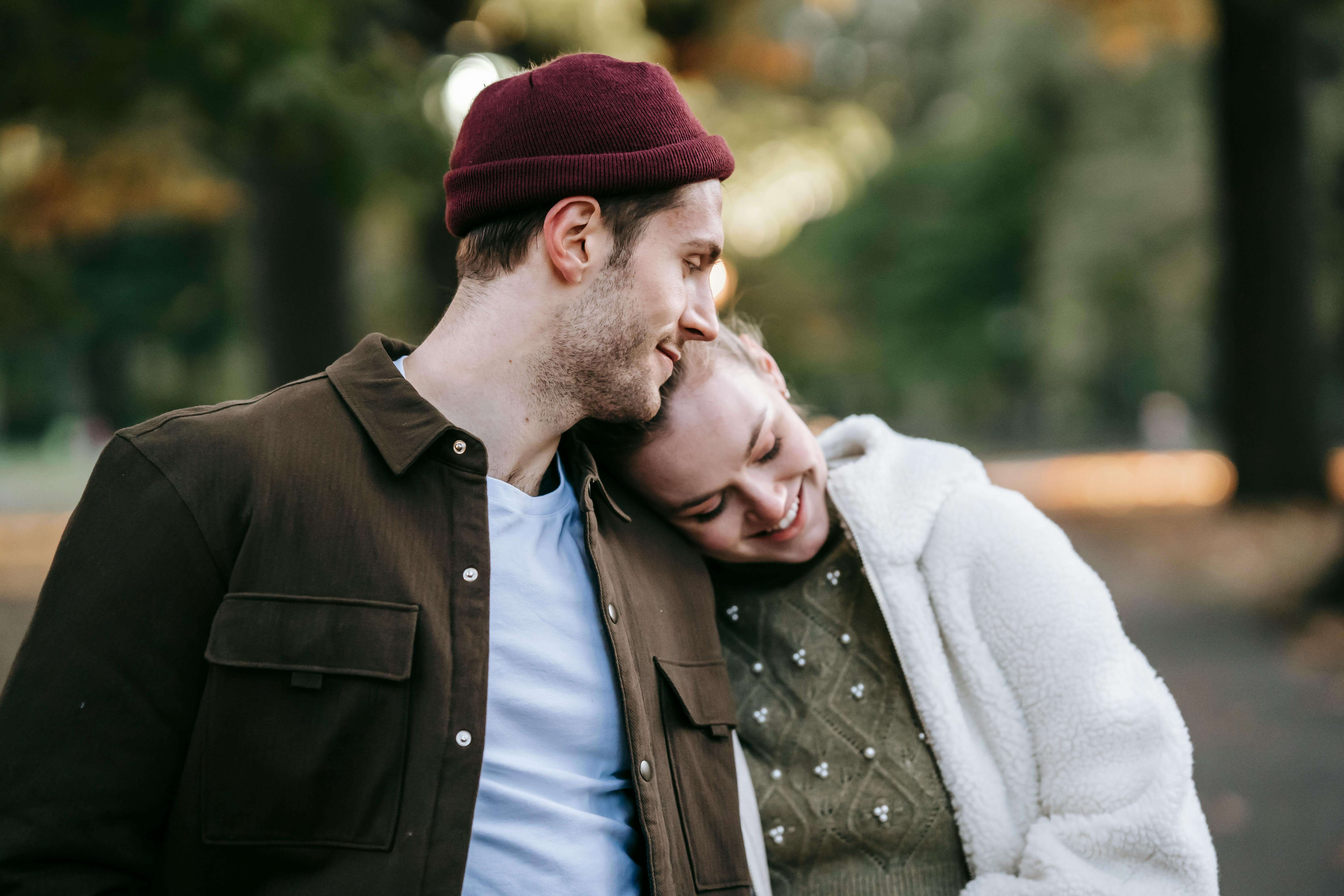 Romantic young couple in stylish warm clothes smiling and embracing during date on sunny autumn day