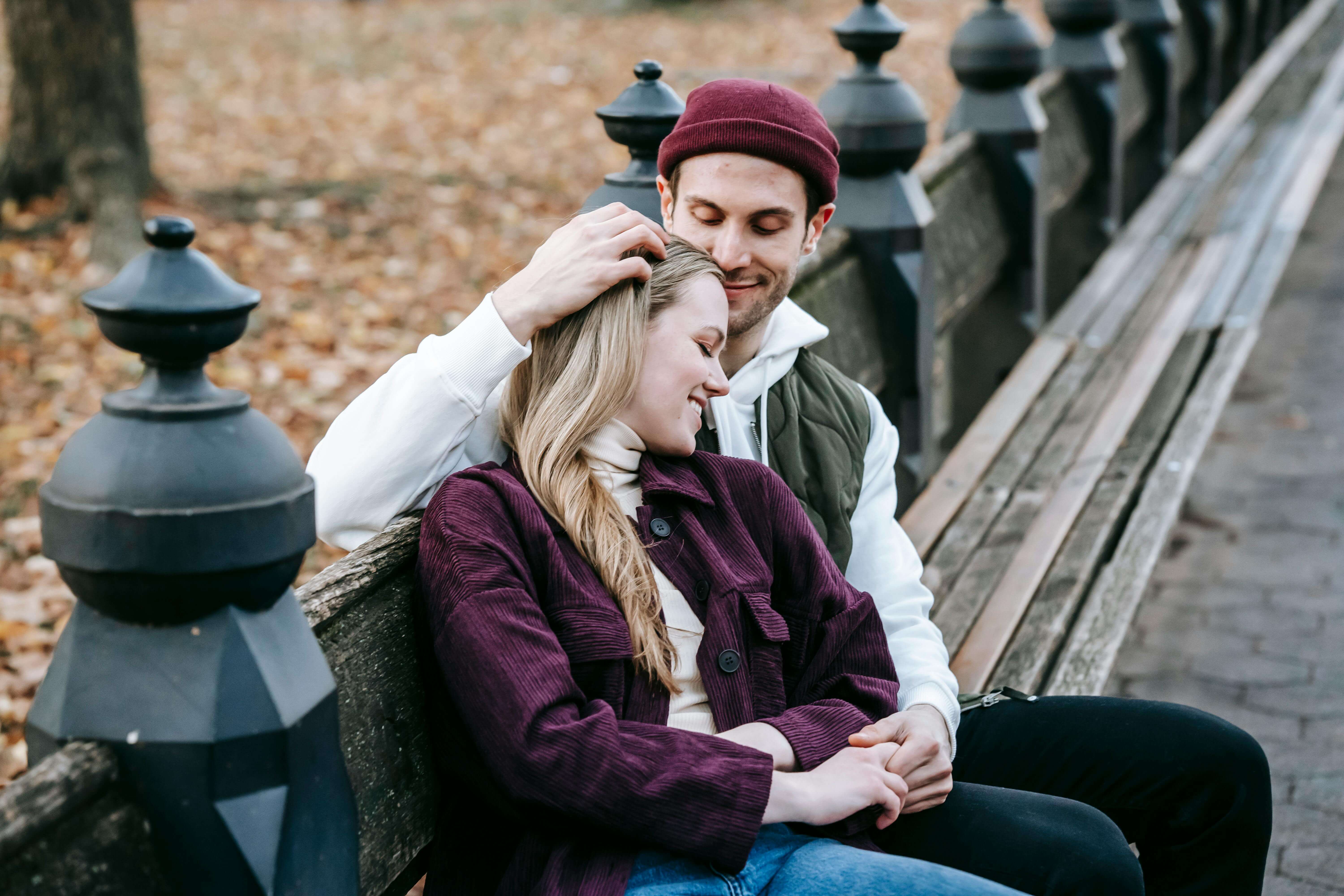 A happy young couple embraces on a park bench surrounded by autumn leaves.