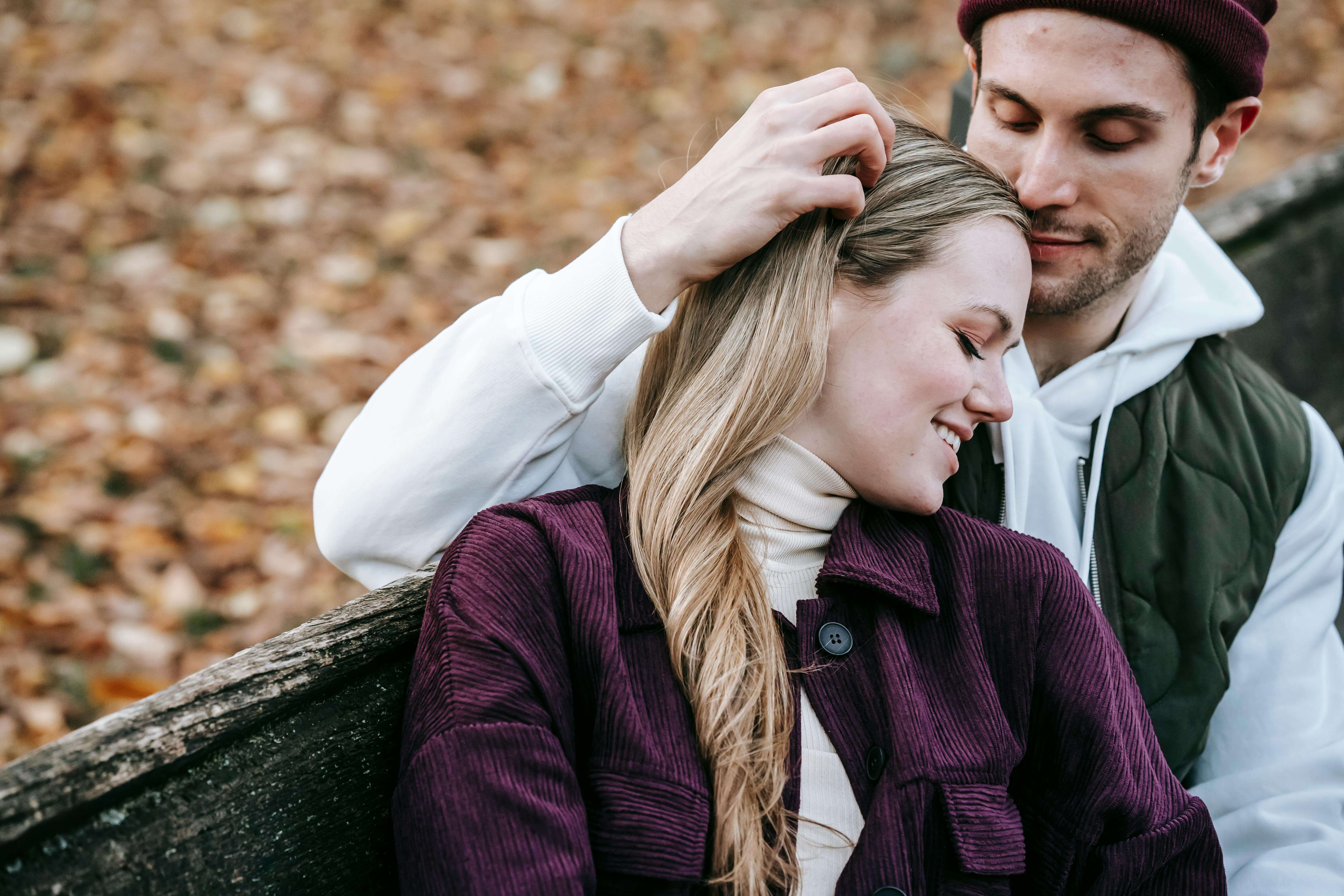 A loving couple embraces on a park bench surrounded by autumn leaves.