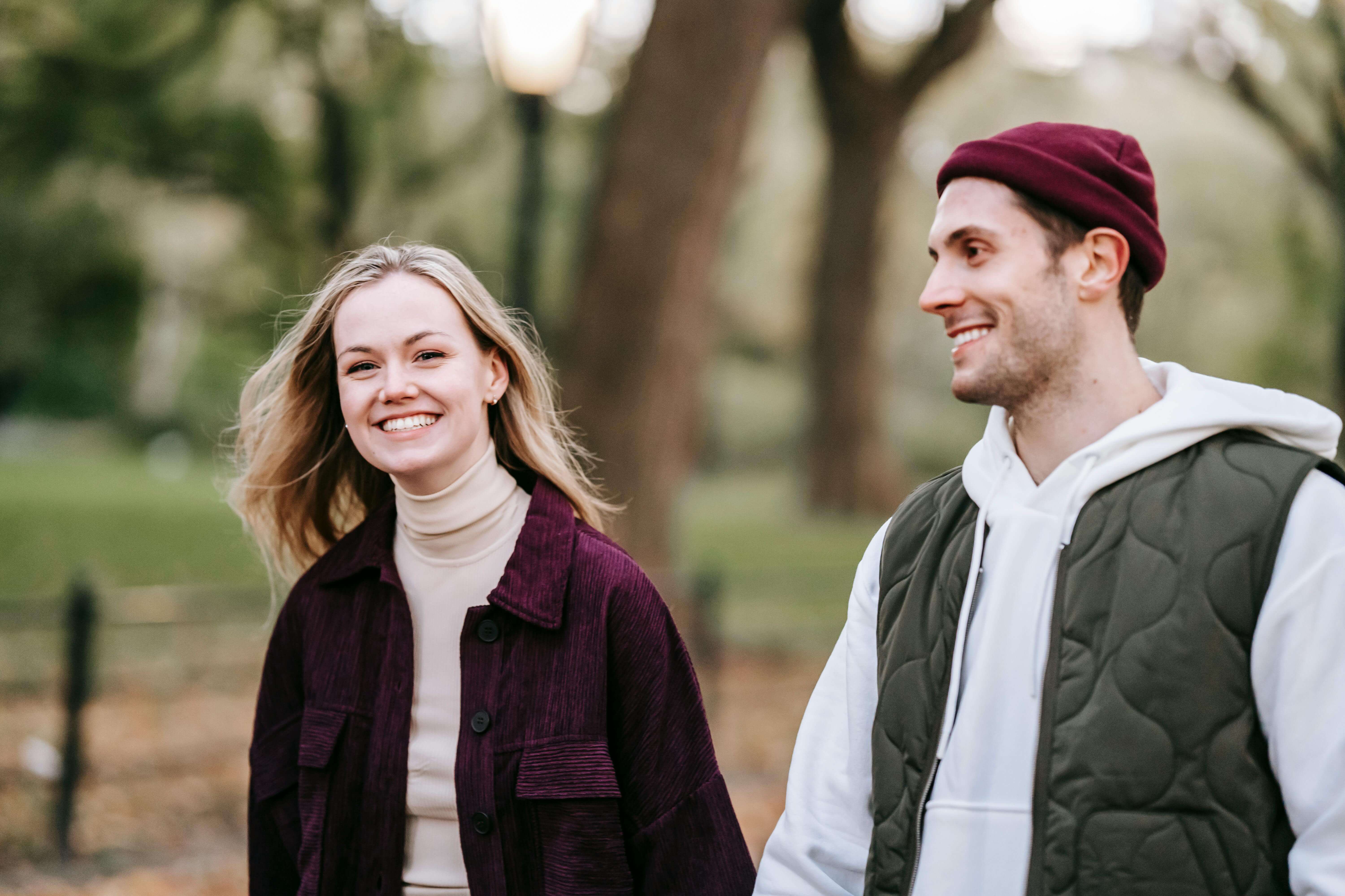 Happy loving young couple in casual warm clothes strolling in autumn park while having date