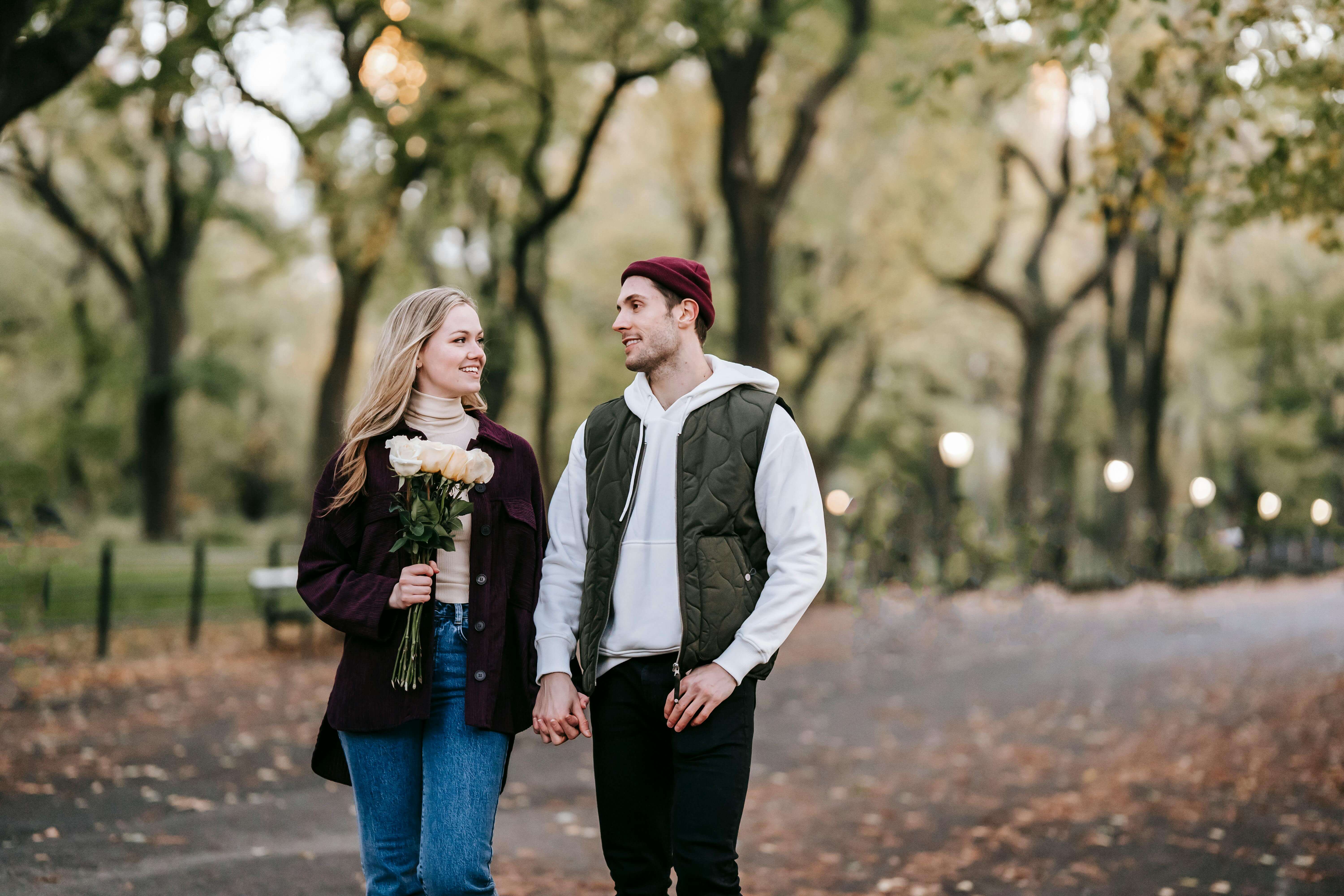 A happy couple holding hands and walking with a bouquet in an autumn park.