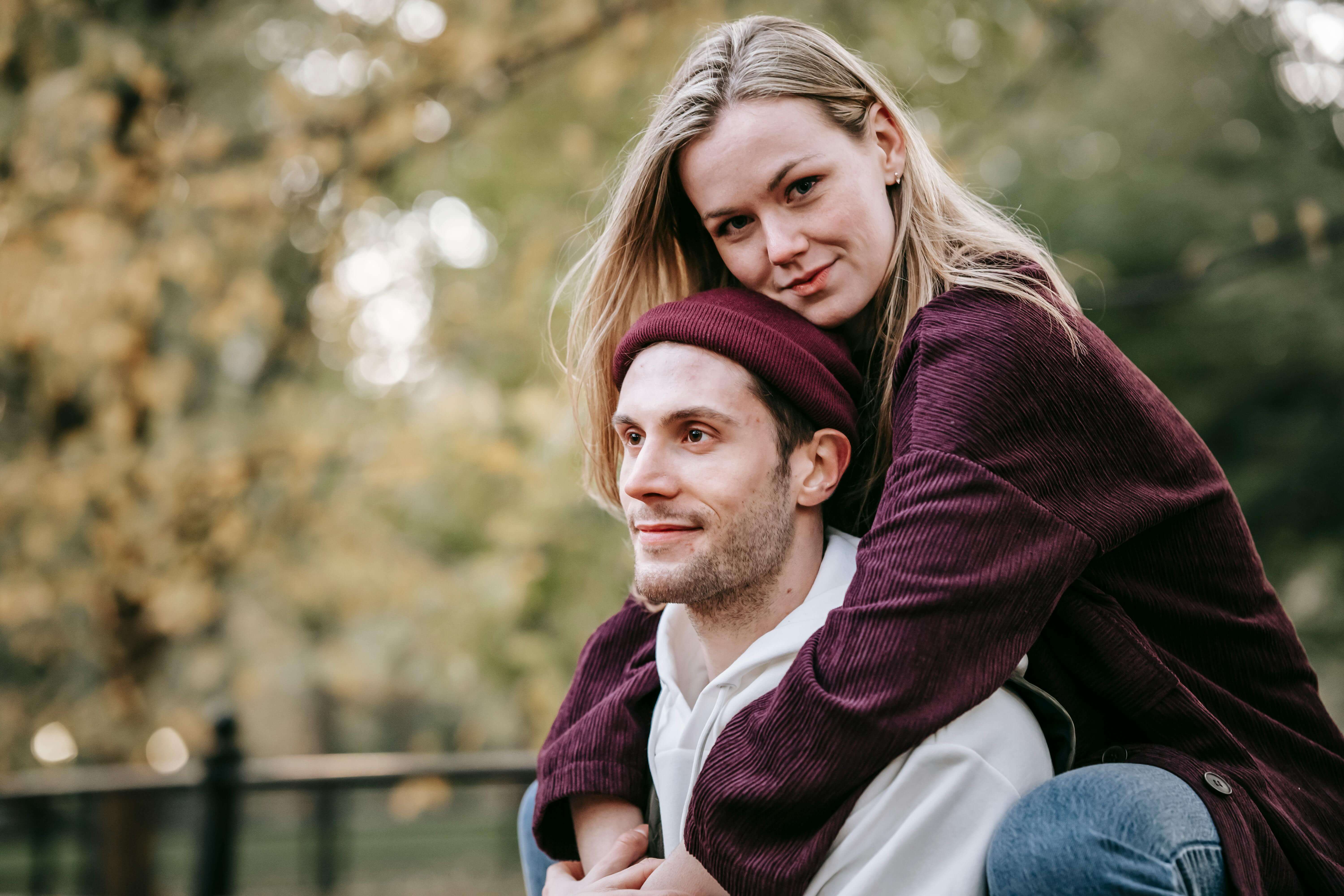 Young charming woman riding piggyback on smiling bearded boyfriend in autumn park in daytime