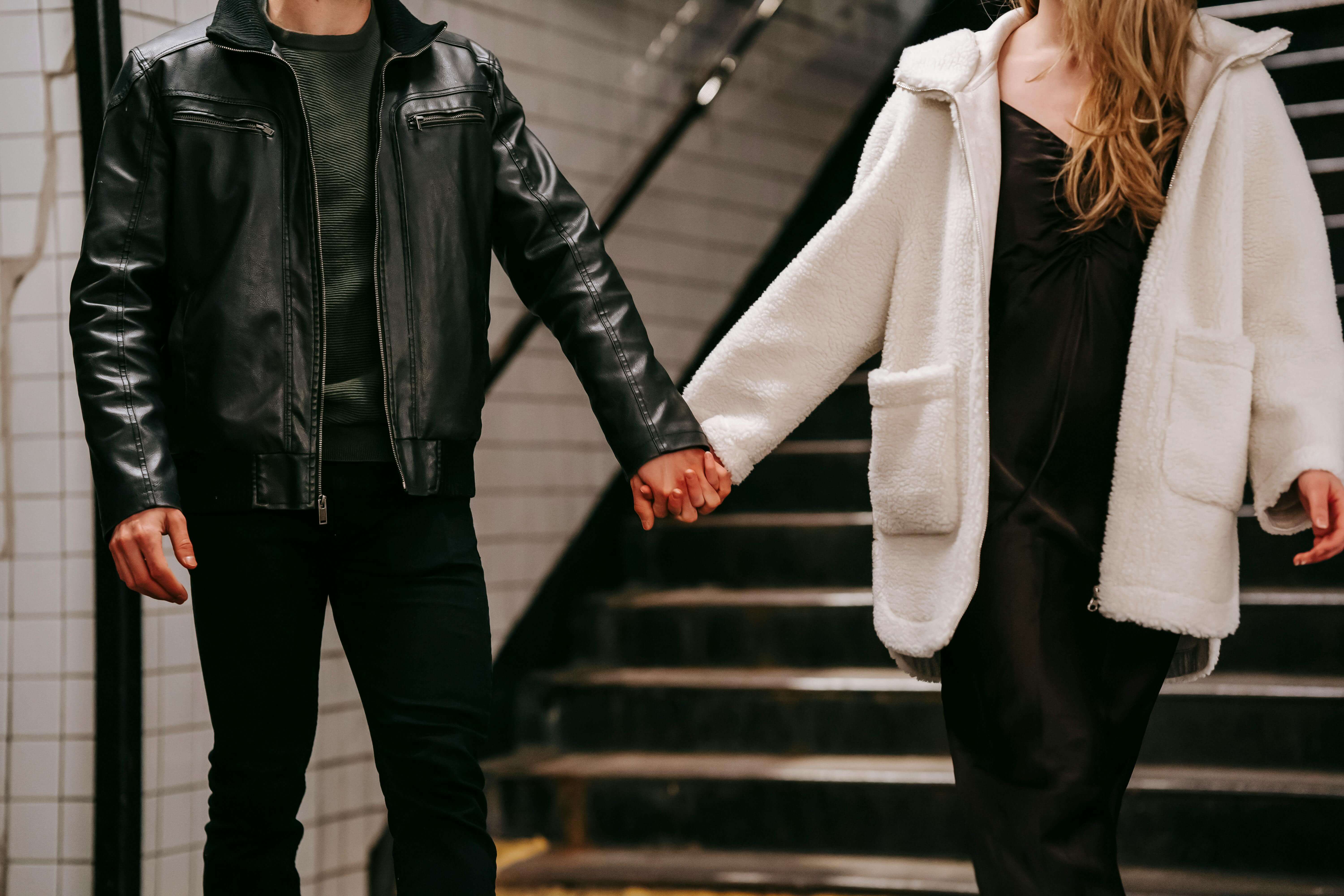 A couple in warm outerwear holding hands on a subway staircase, emphasizing affection.