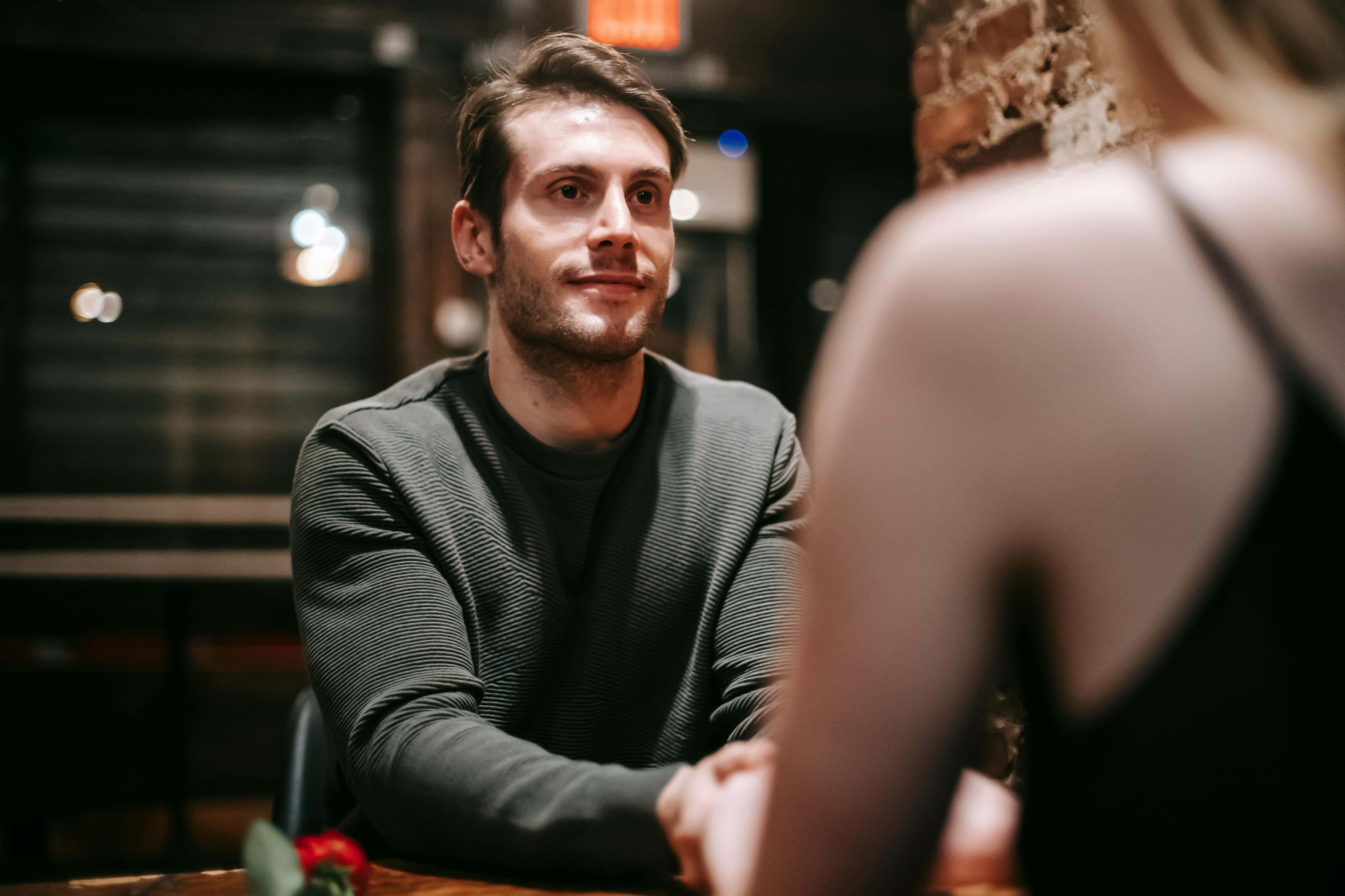 Young man in casual clothes sitting at table in modern cafe with girlfriend