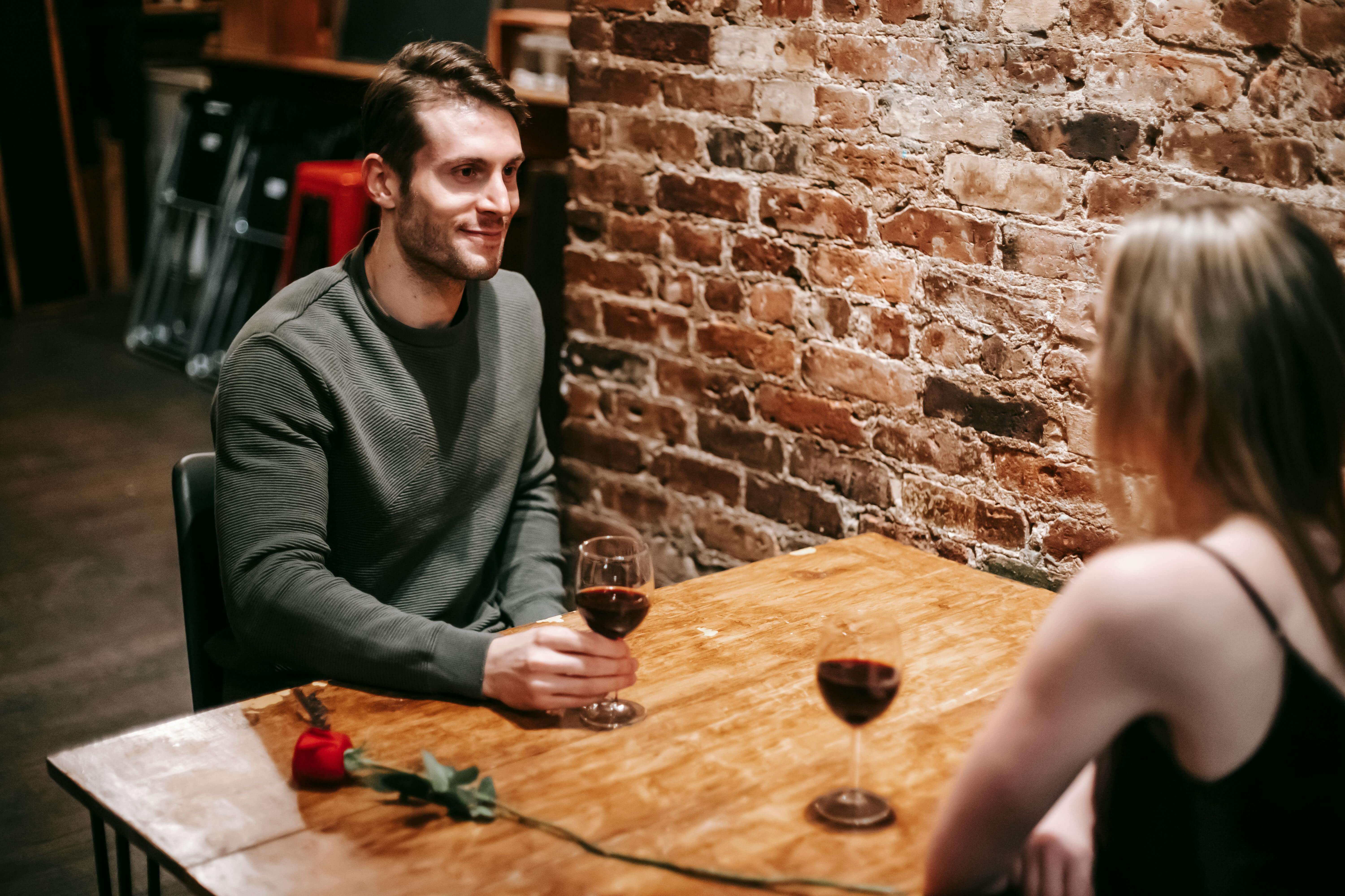 Couple enjoying a romantic evening with red wine and intimate conversation in a cozy restaurant setting.