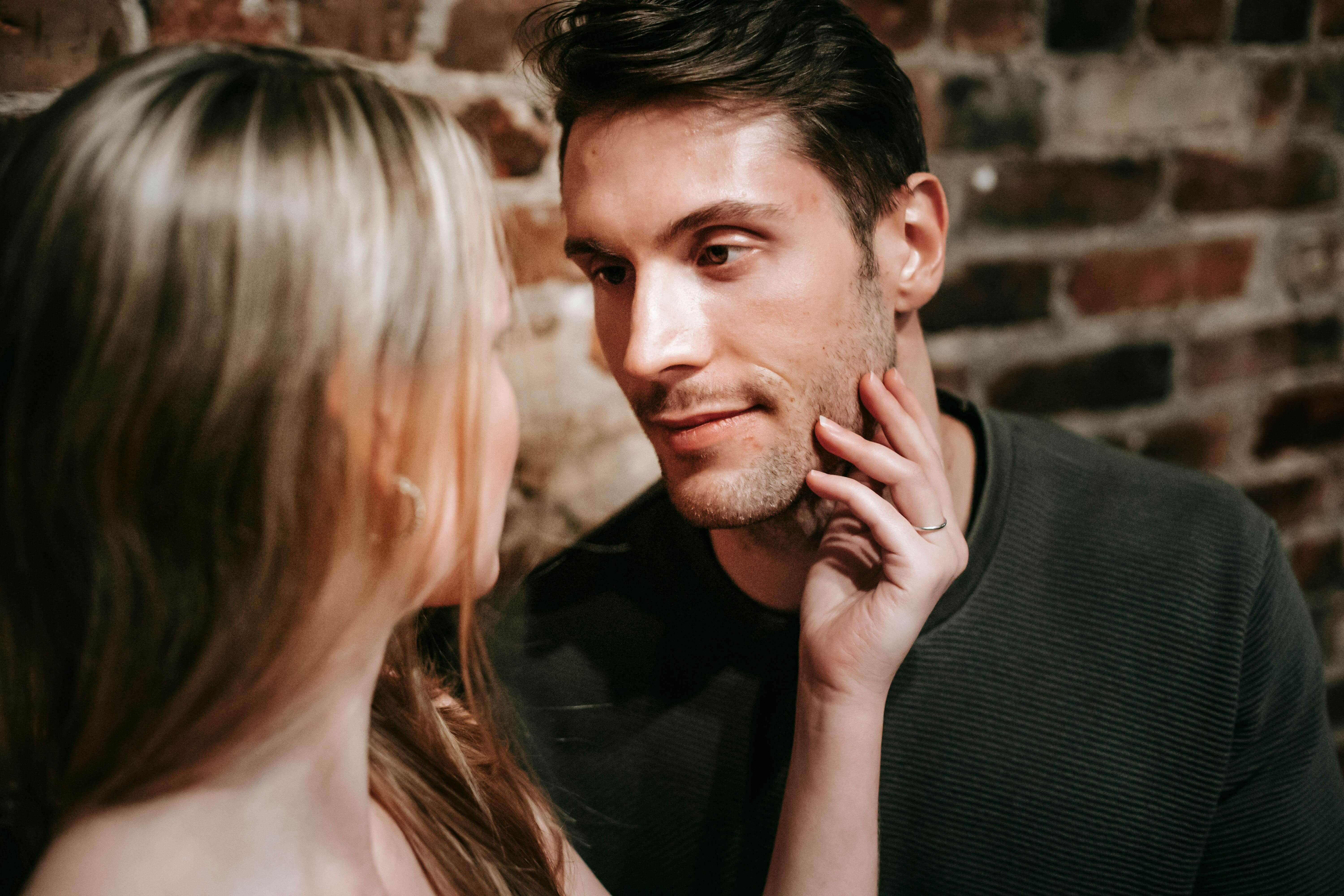 A couple in love gazing affectionately at each other in a cozy setting with a brick wall backdrop.
