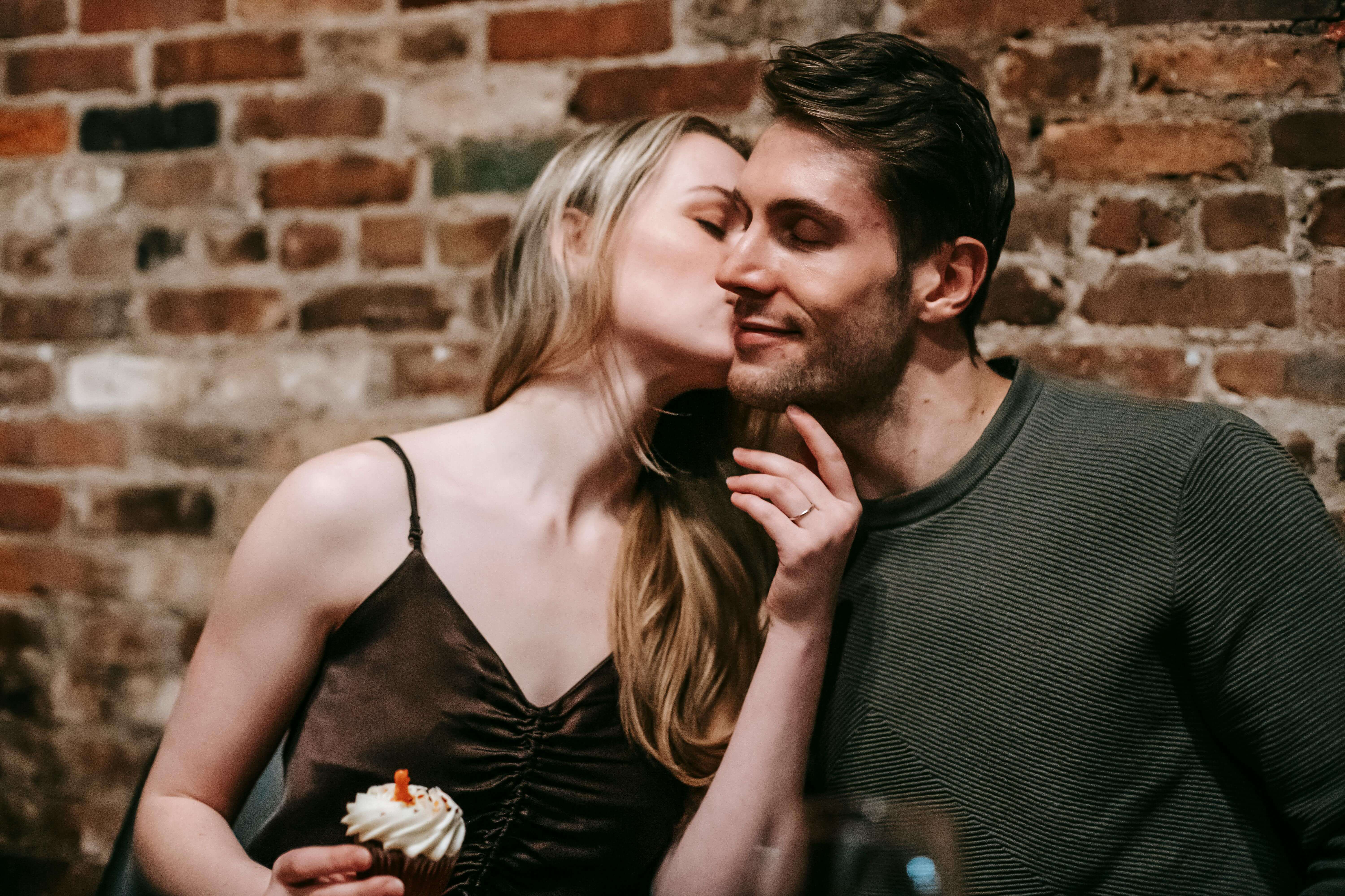 Sweet moment of a couple sharing a tender kiss at a romantic dinner with cupcakes.