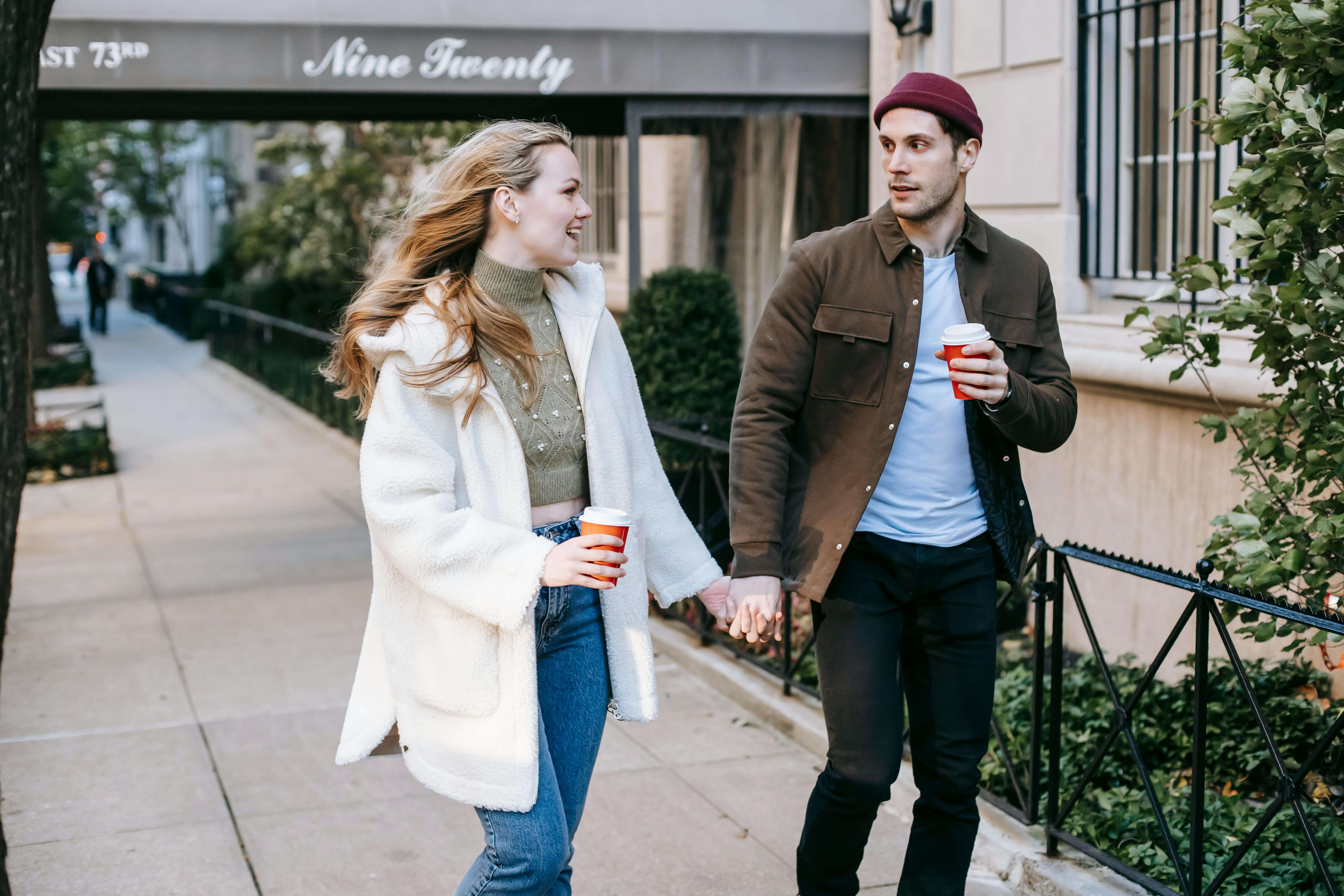 Young couple holding hands and enjoying a coffee while strolling on a city street.