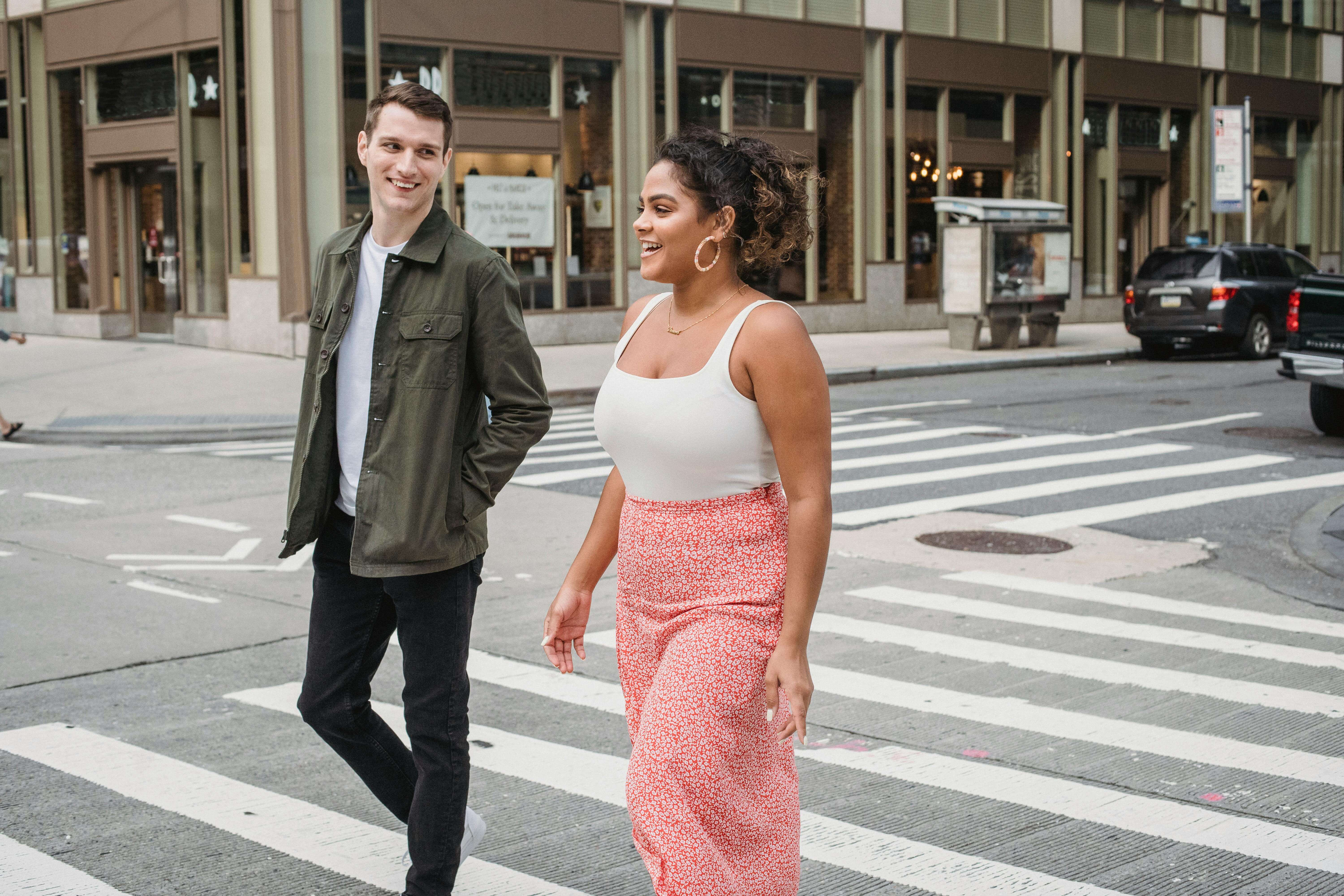 Happy young couple walking across a city crosswalk, enjoying a lively daytime stroll together.