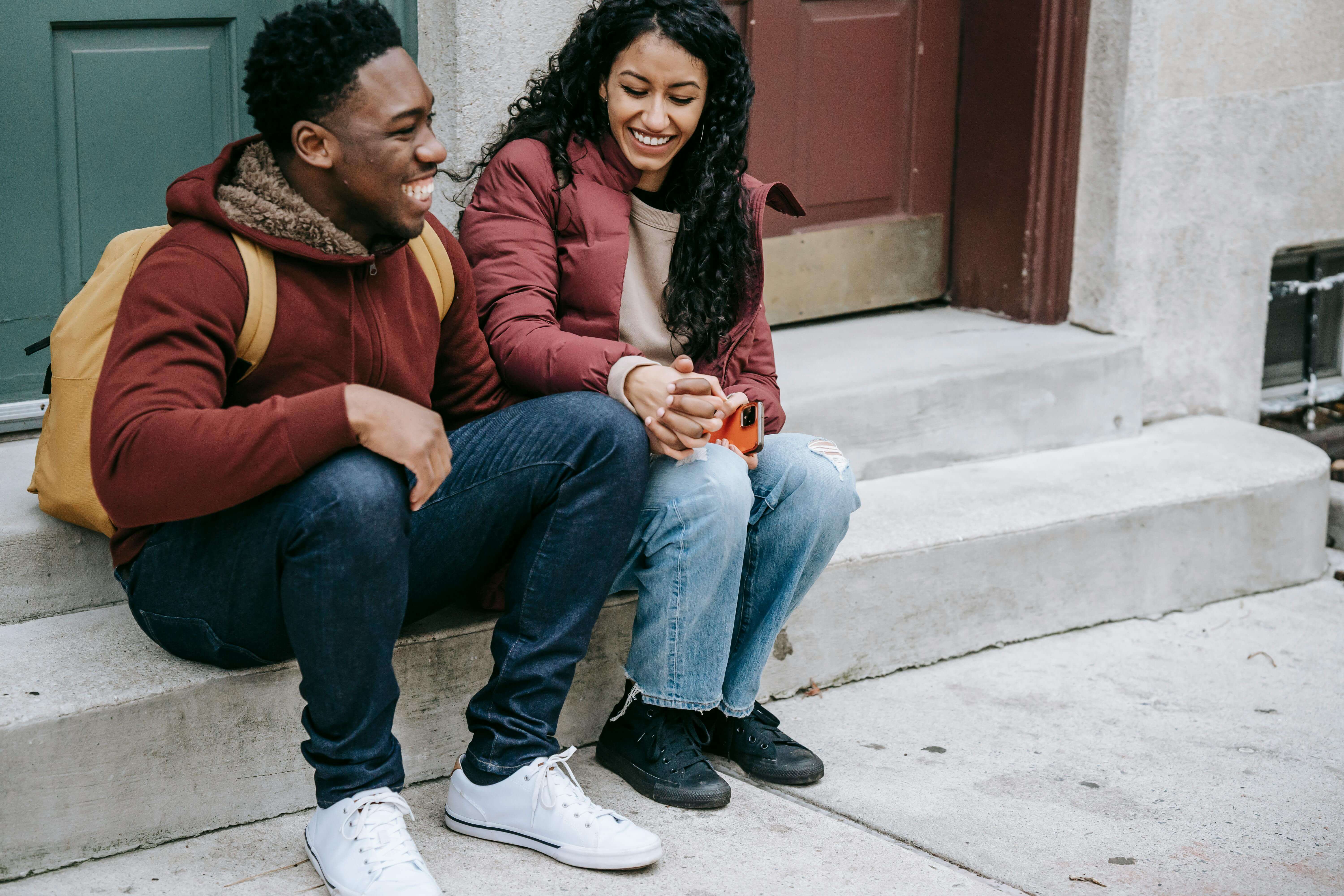 Cheerful multiethnic crop couple laughing and smiling while holding hands and resting on concrete steps