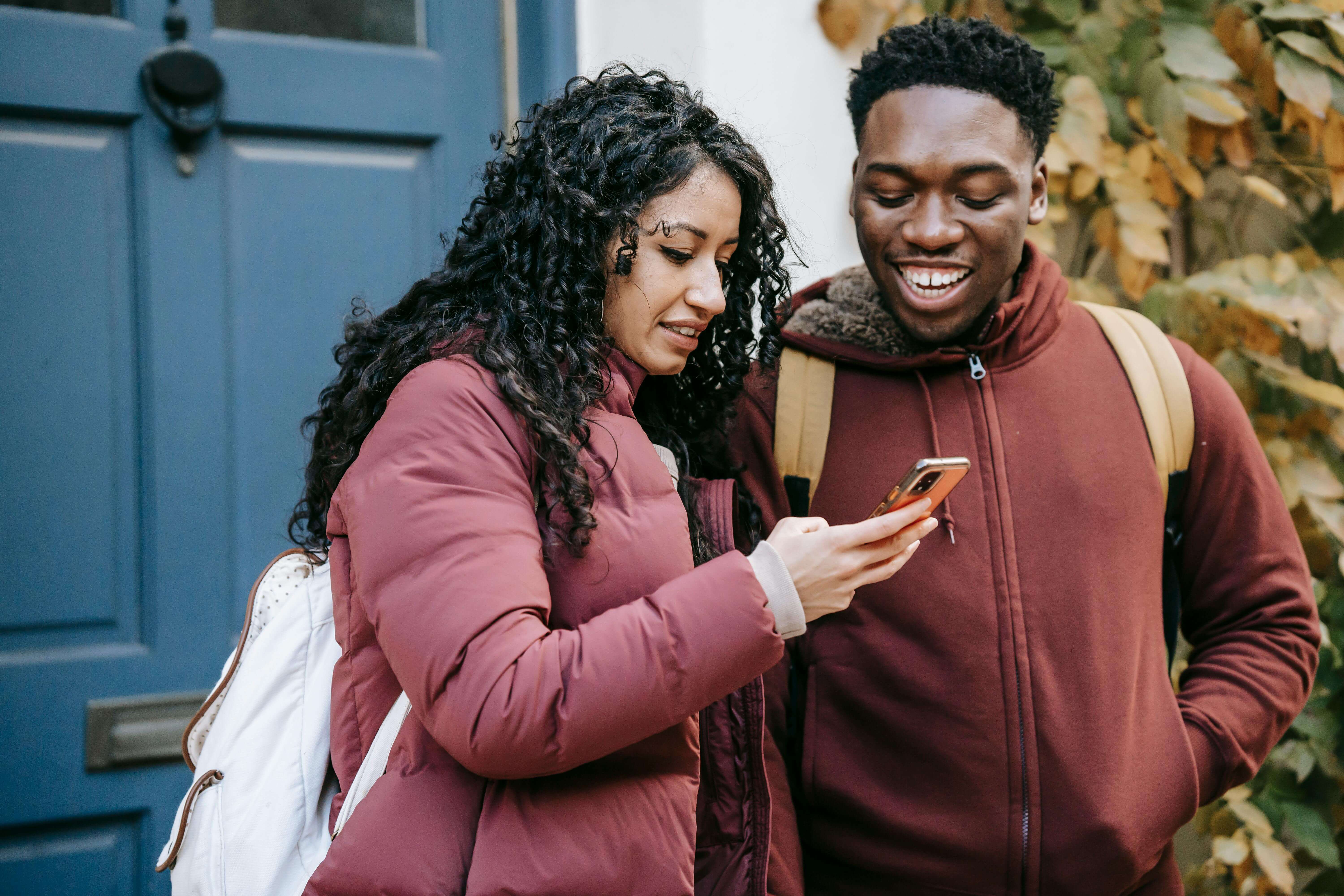 Smiling couple interacting with a smartphone outside a building, enjoying a cheerful moment.
