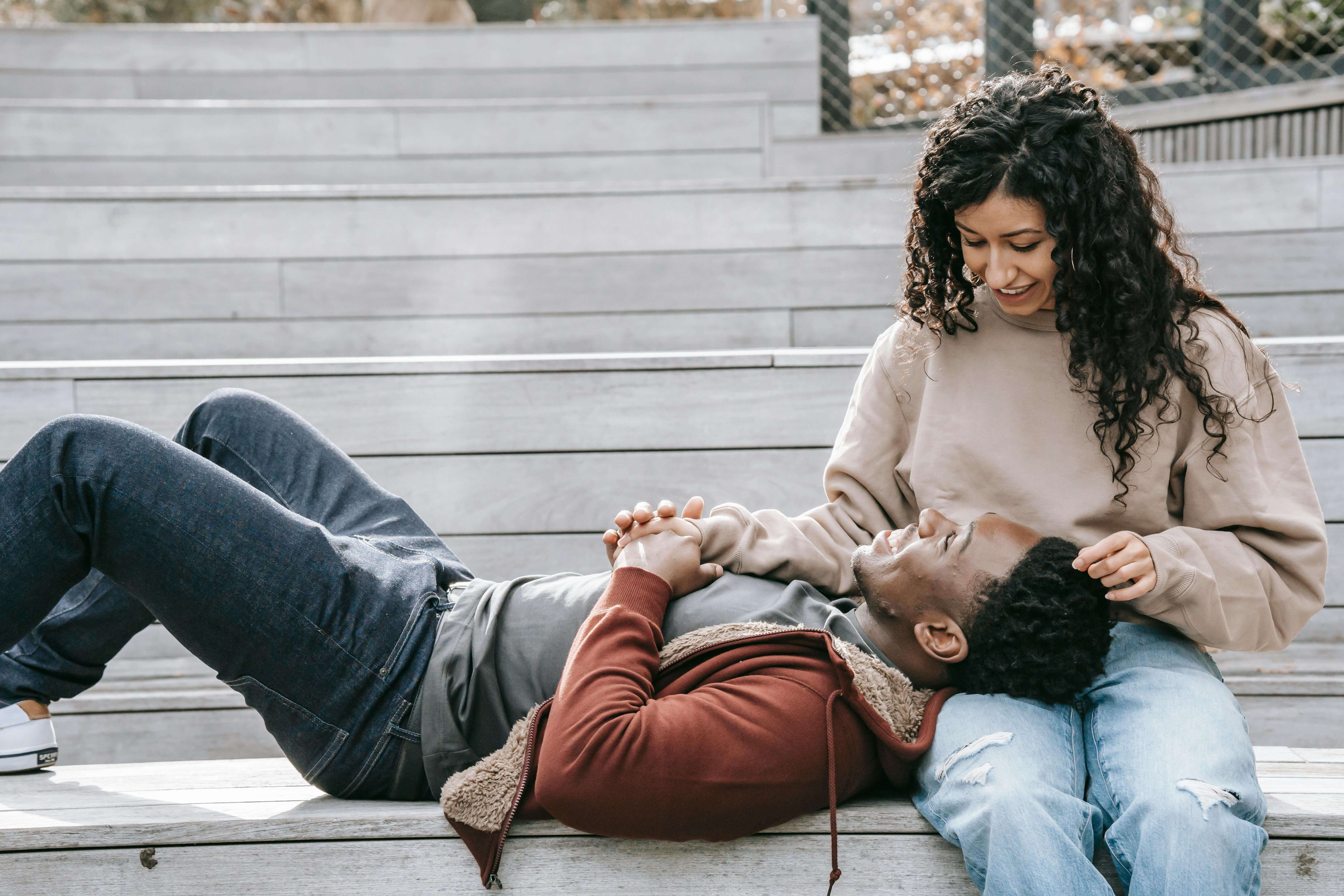 A happy multiracial couple shares a tender moment on outdoor stairs, enjoying each other's company.