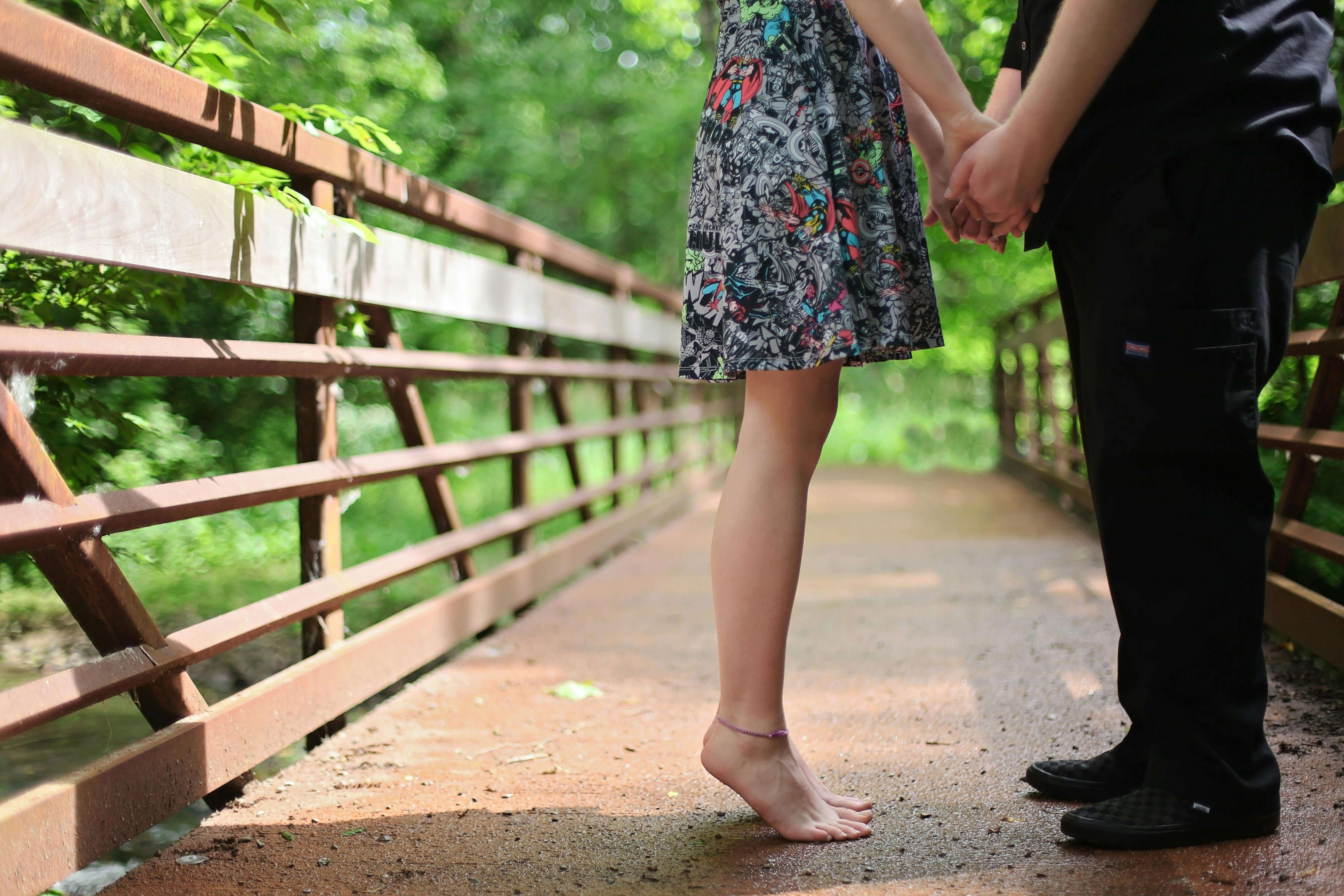 A barefoot couple holding hands on a wooden bridge in a lush green setting, symbolizing romance.