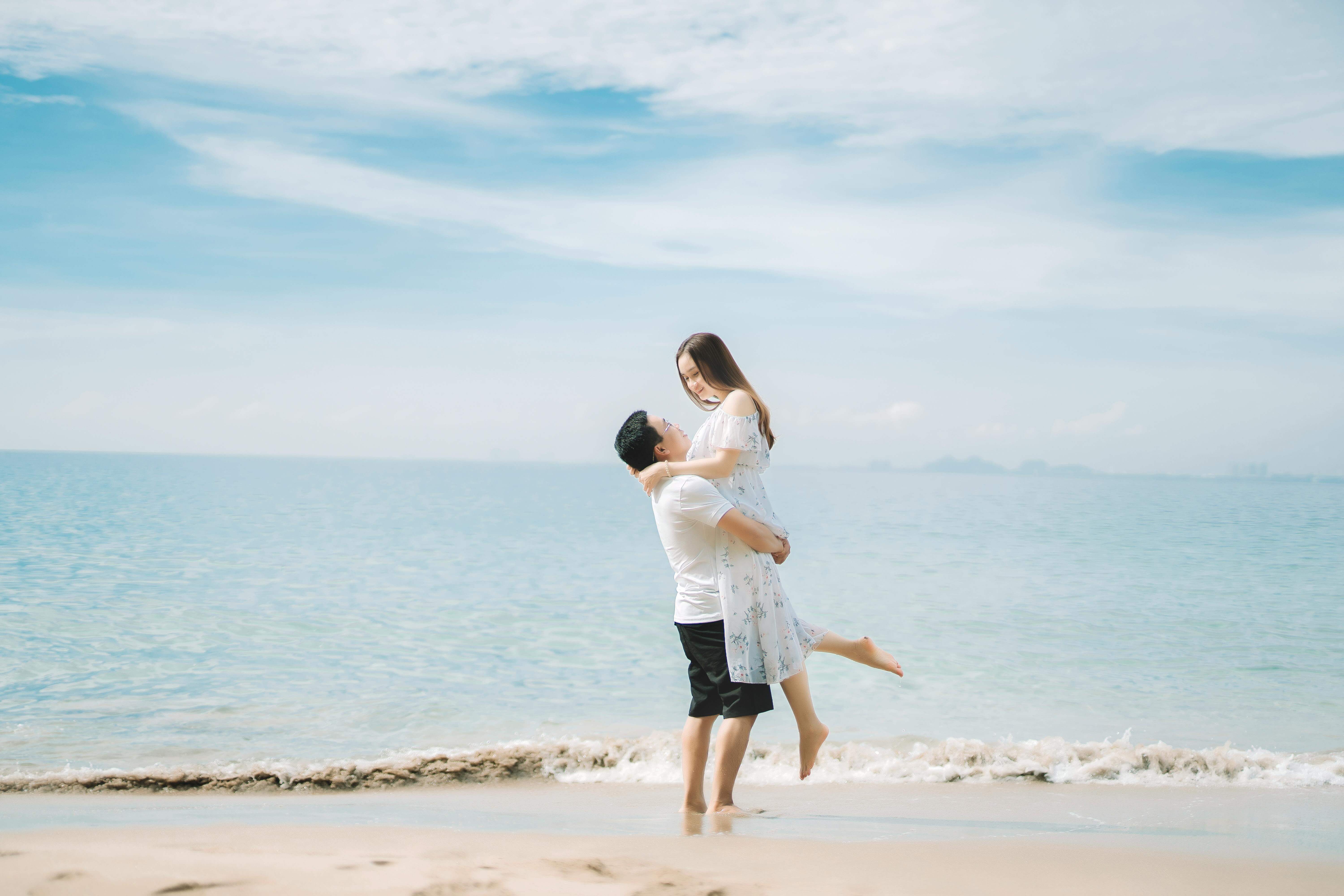 A happy couple shares a joyful moment at the beach during a sunny day.