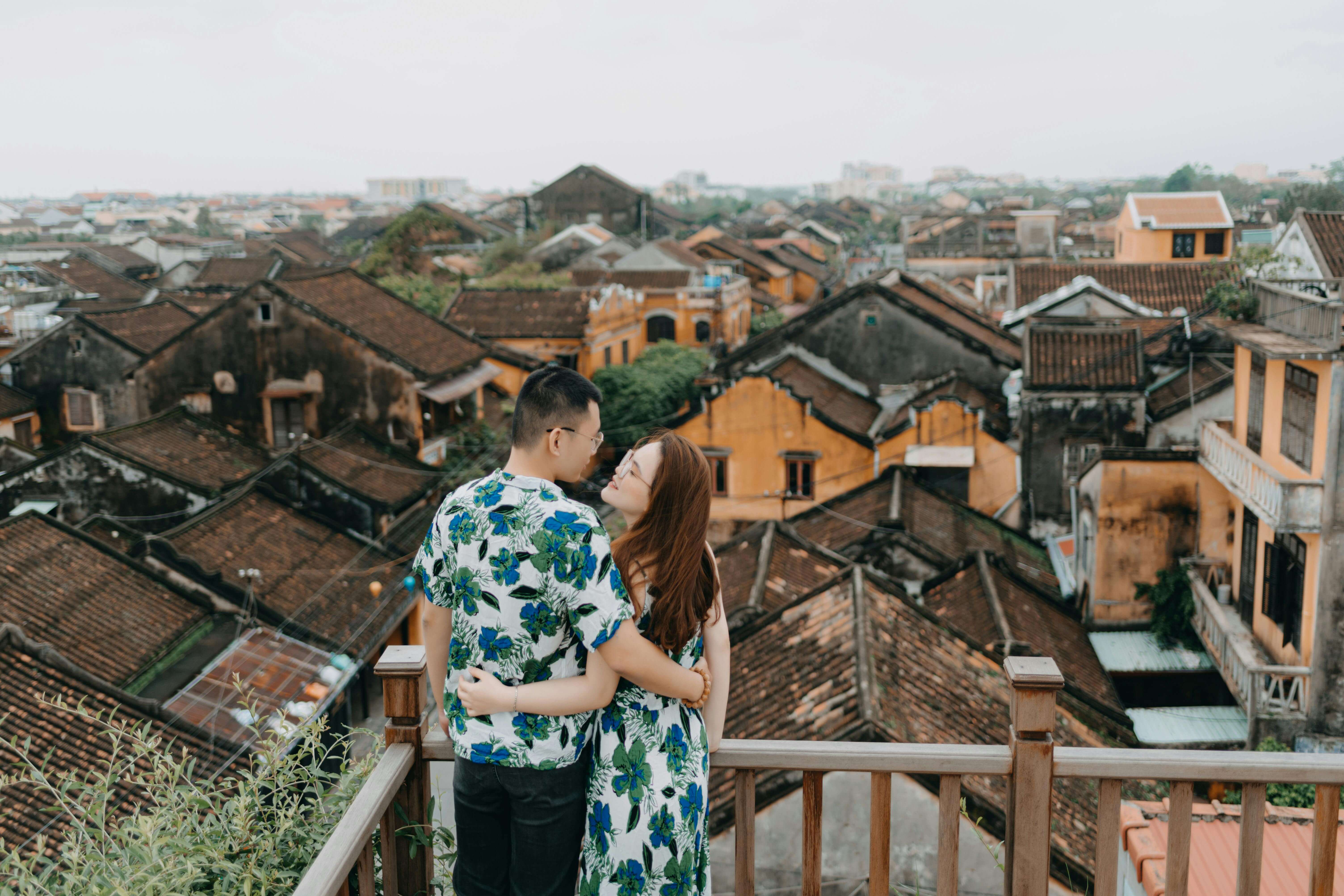 A couple embraces on a rooftop terrace overlooking ancient roofs in a romantic setting.