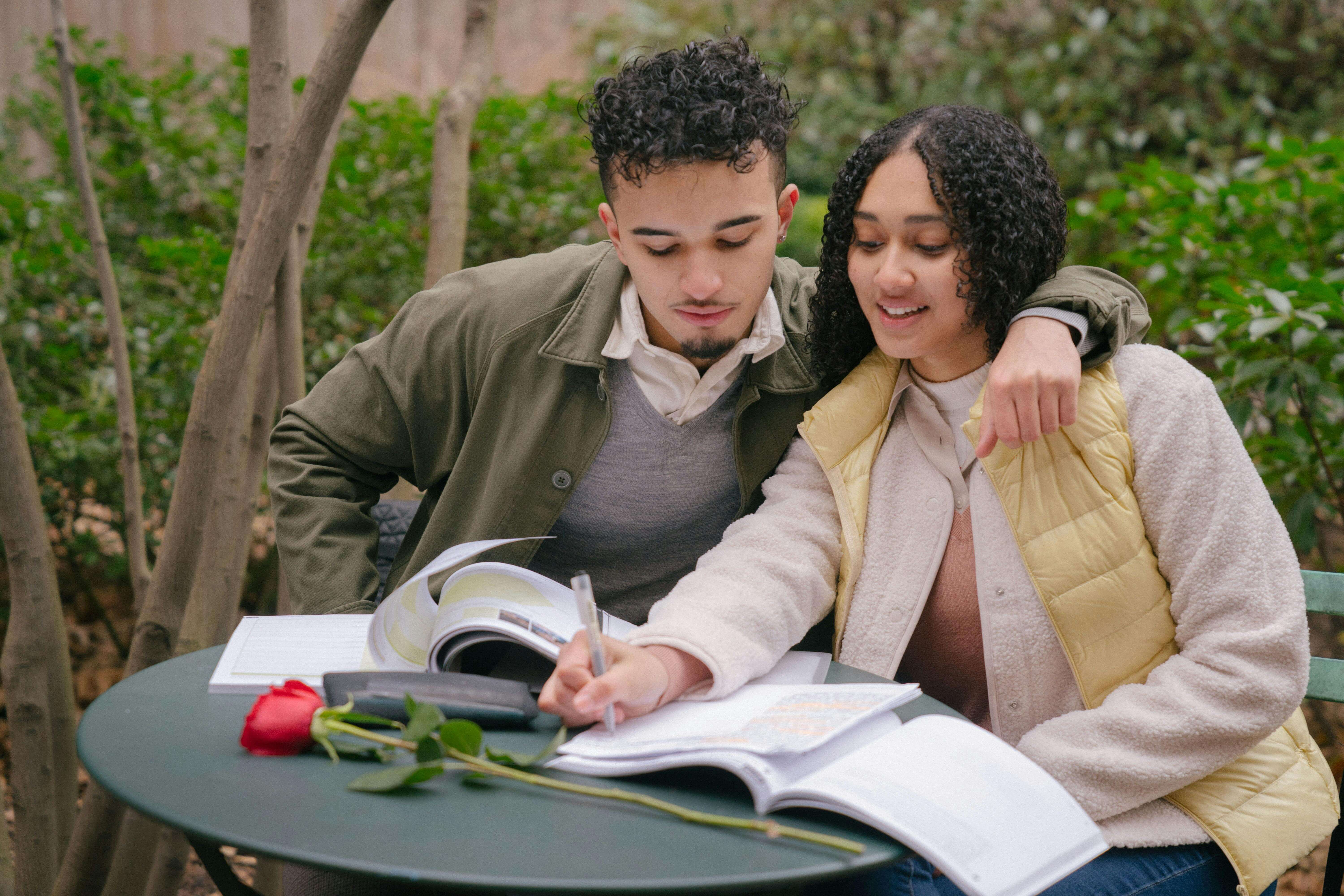 A couple embraces while studying in a park, showcasing romance and education.