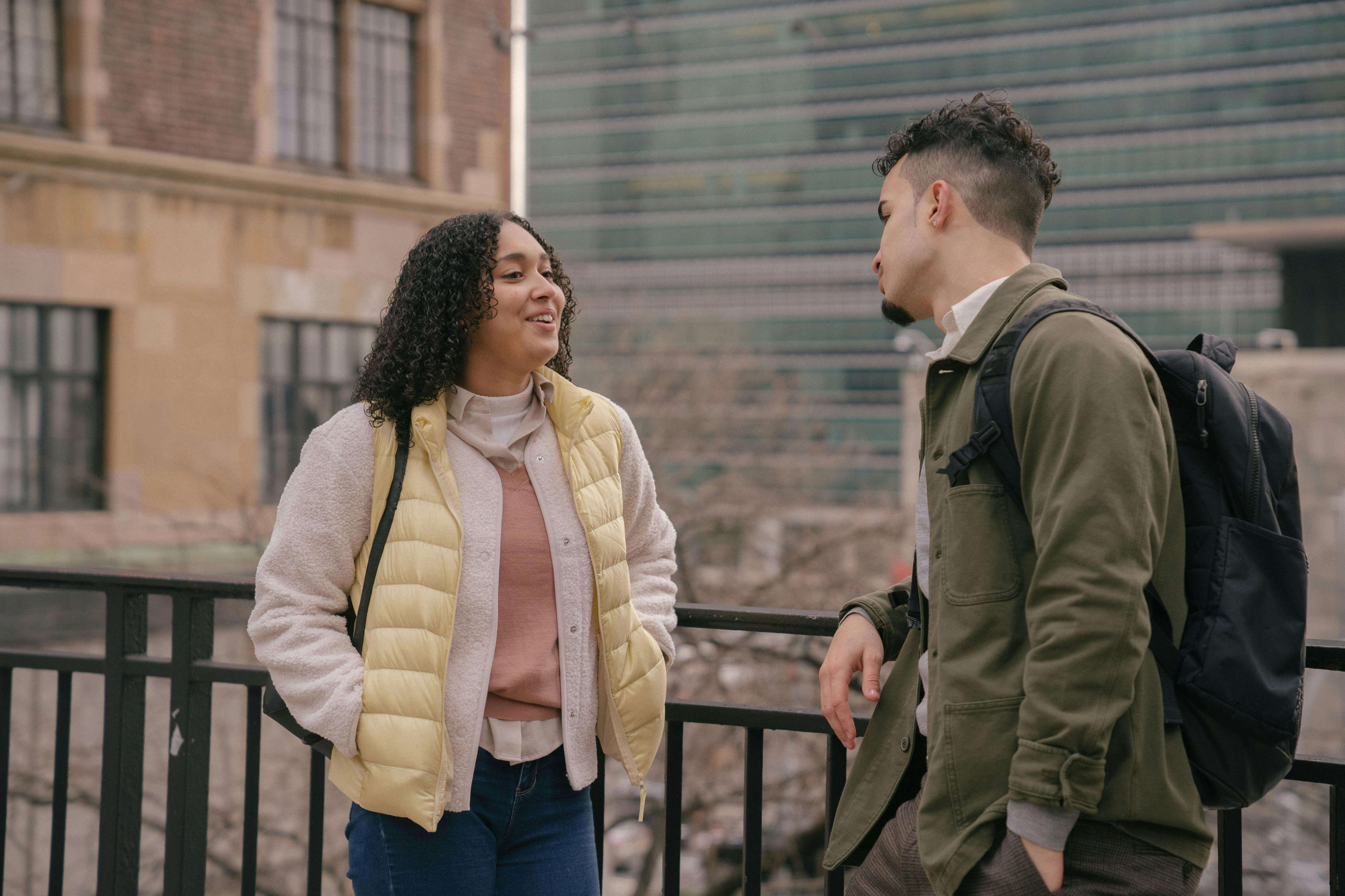 Happy Hispanic girlfriend and boyfriend speaking while leaning on metal railing on street of town