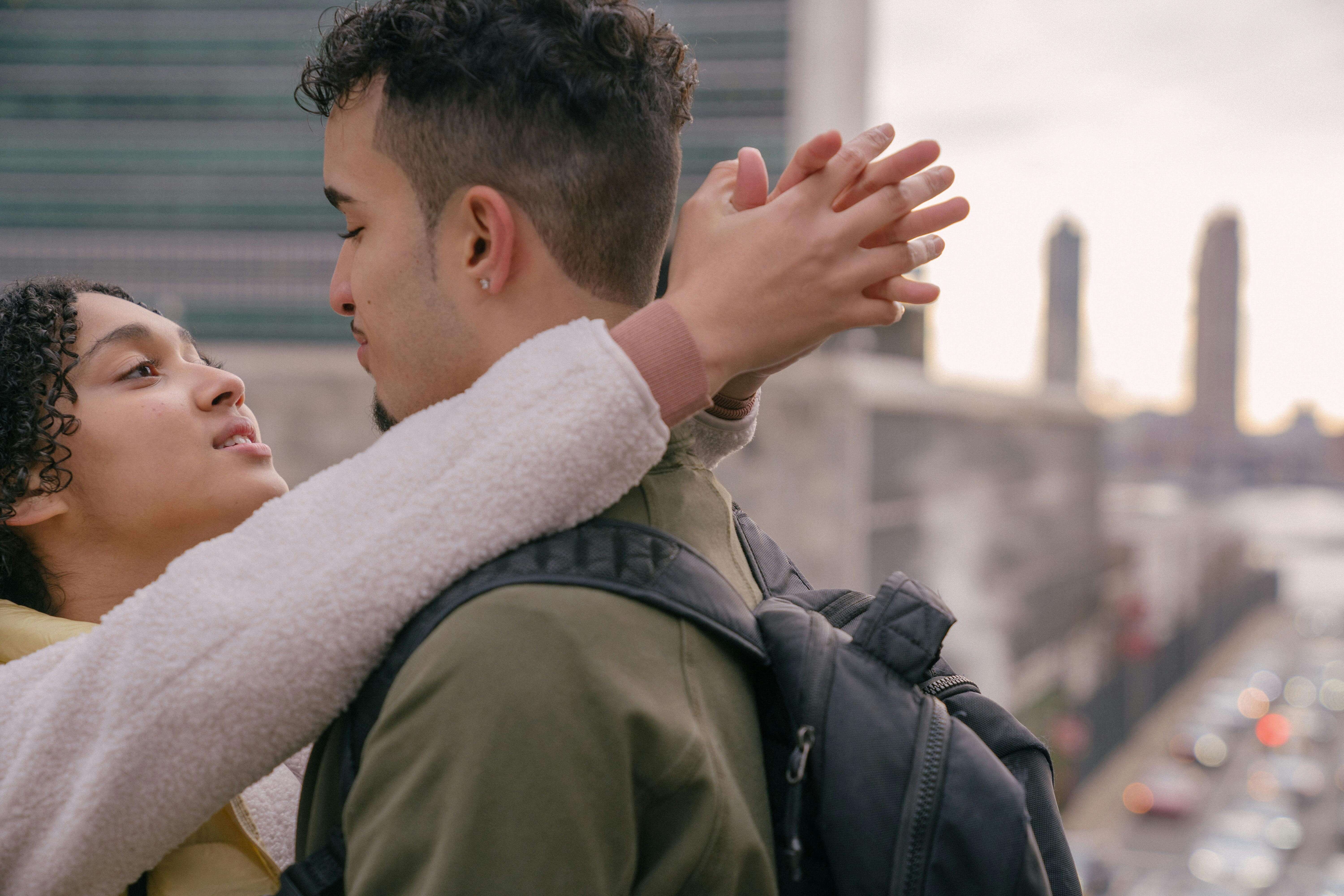 Young couple embracing outdoors against a cityscape backdrop, expressing affection and romance.