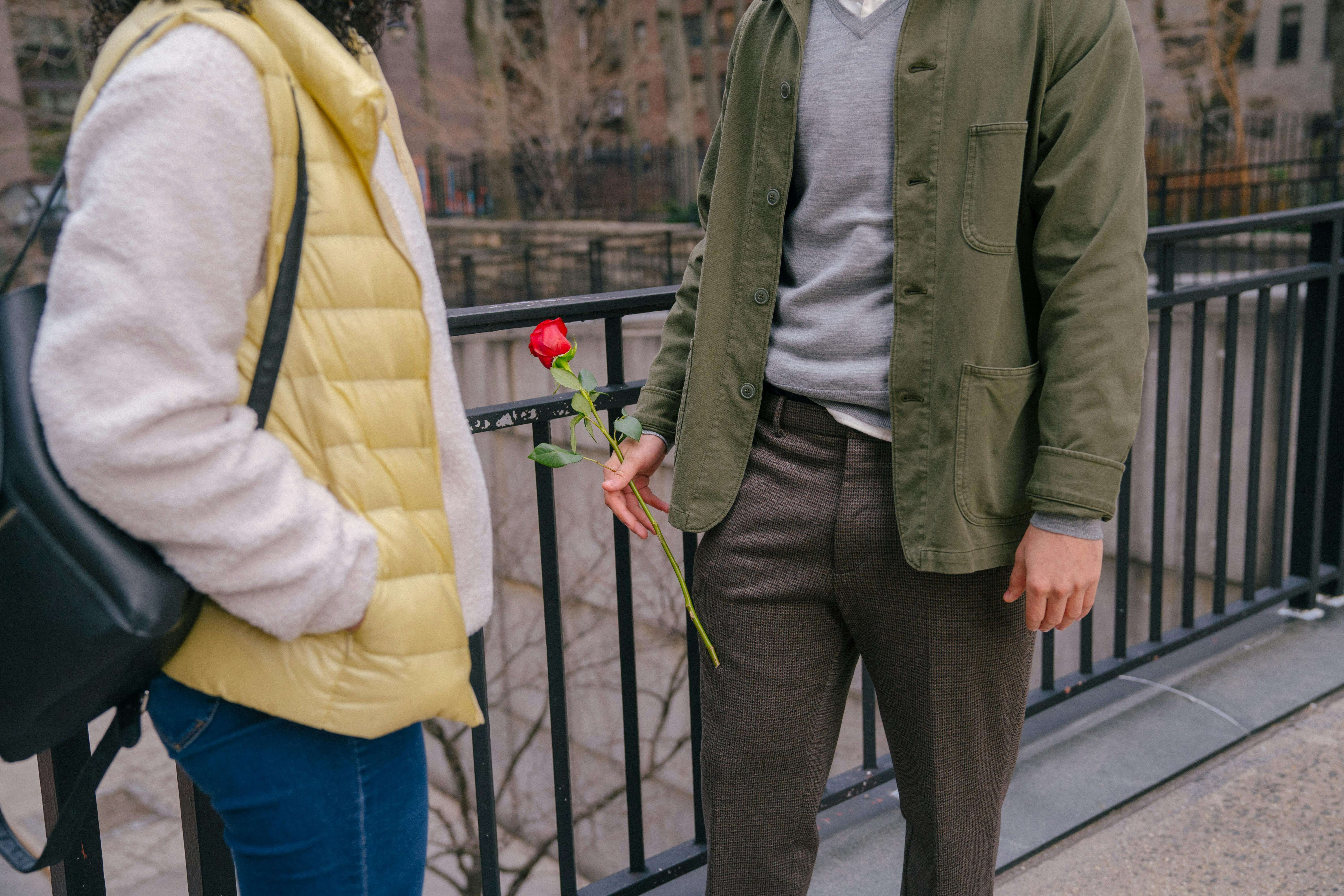 A romantic moment as a young couple exchanges a rose in an urban outdoor setting, showcasing affection and style.
