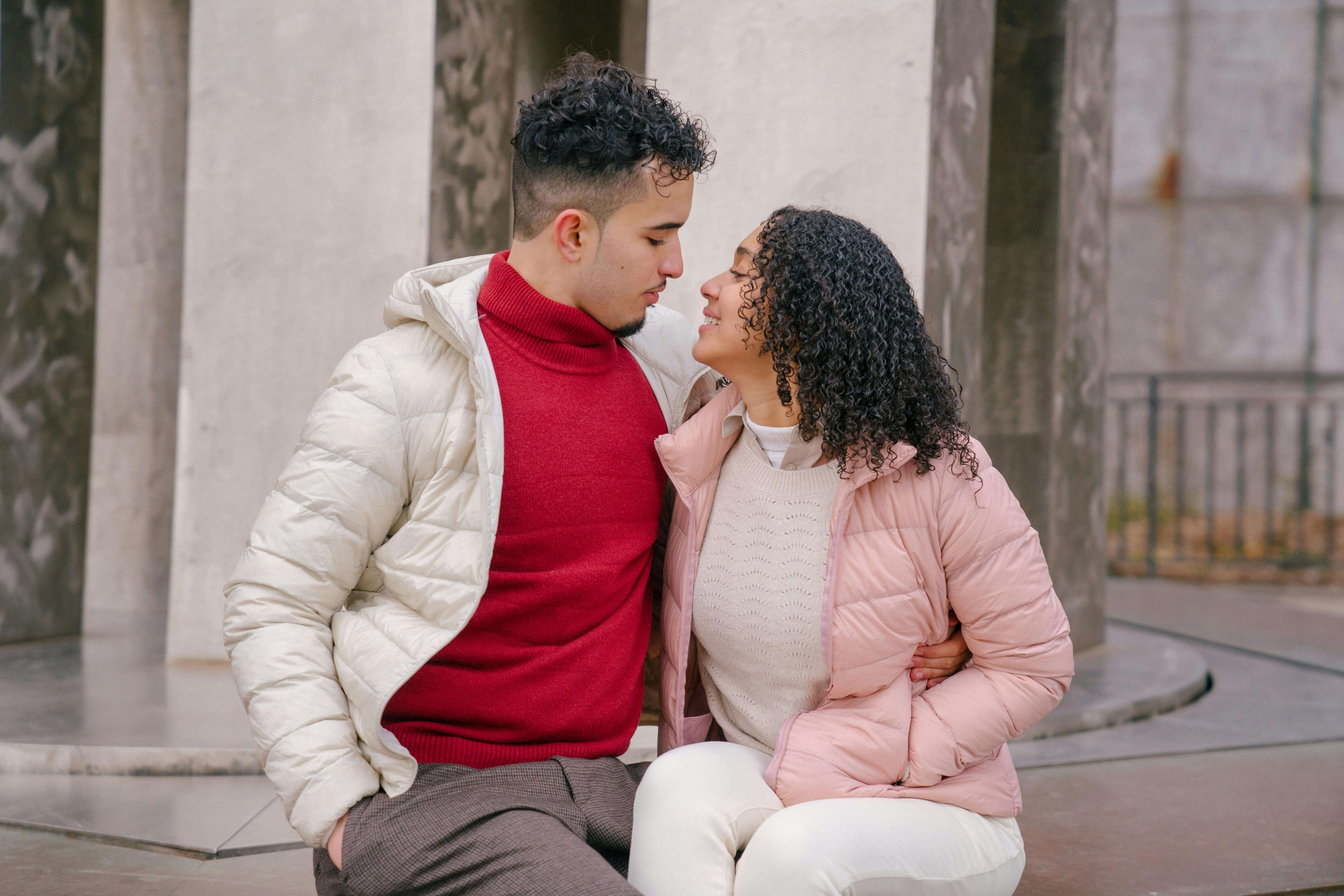 Young couple enjoying a warm embrace in a park setting wearing winter jackets, creating a romantic autumn atmosphere.