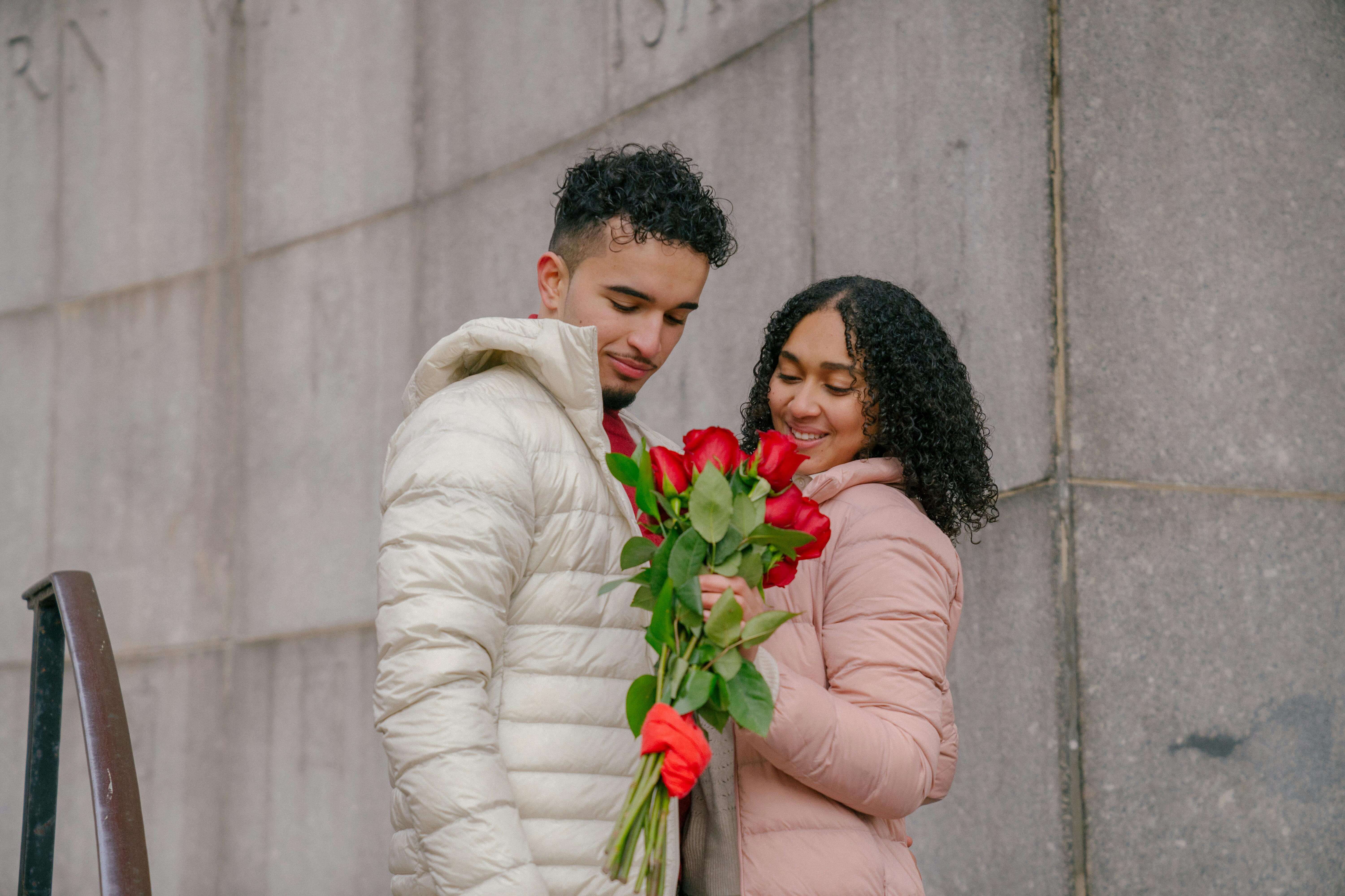 Couple sharing a joyful moment with red roses outside, expressing love and happiness.