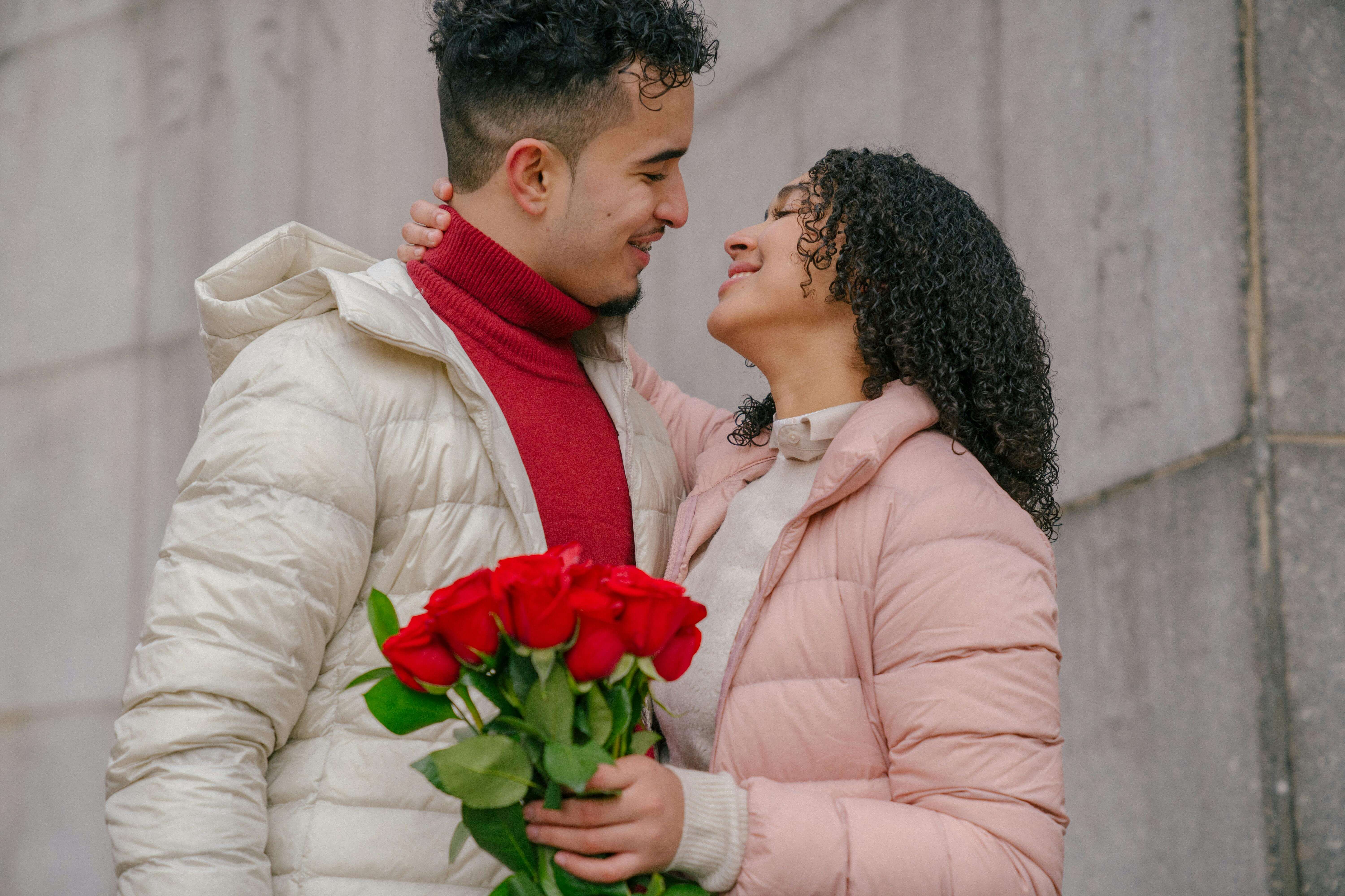 A joyful couple embracing with a bouquet of red roses, celebrating love and romance outdoors.