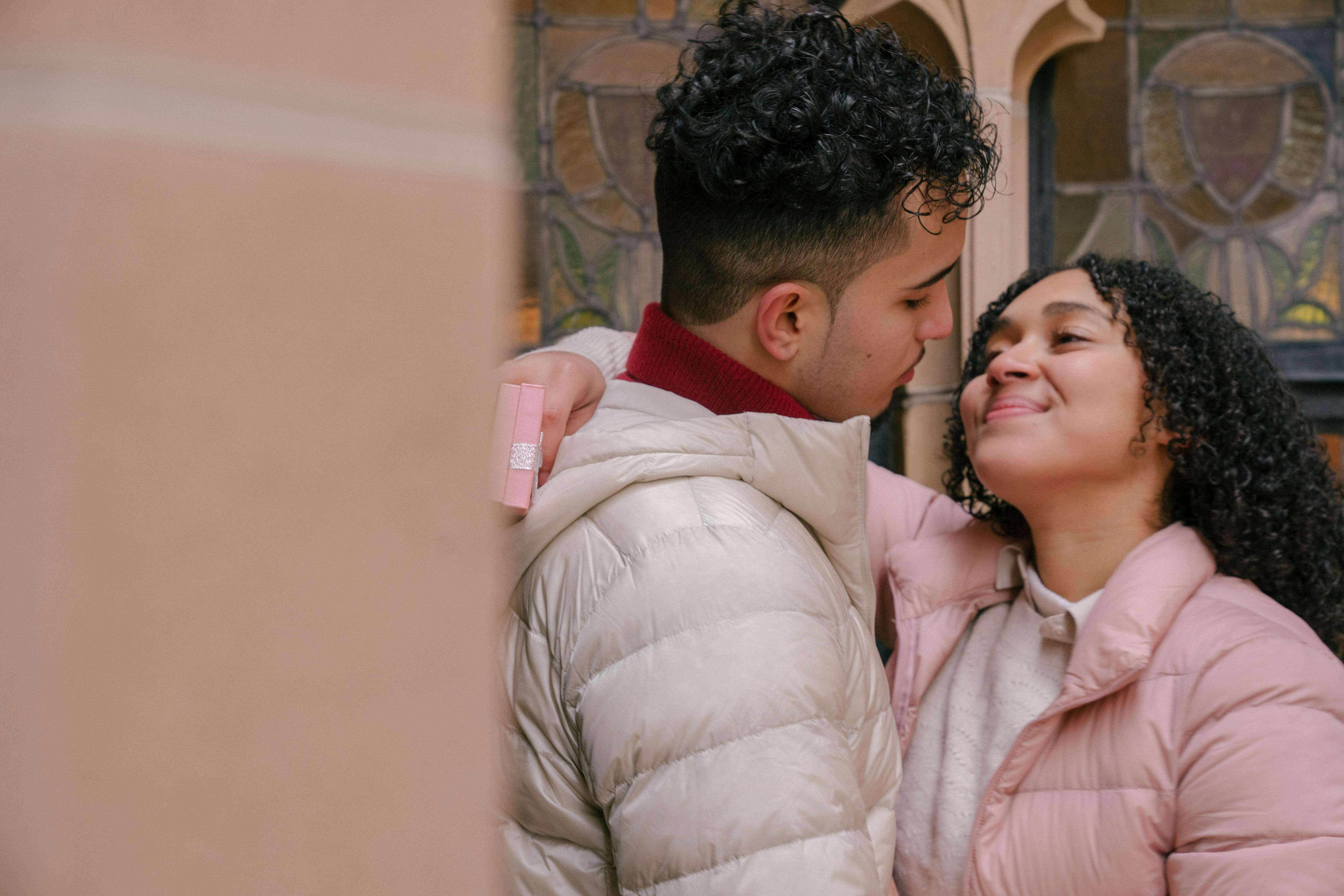Cheerful Hispanic couple embracing and looking at each other on city street in daytime