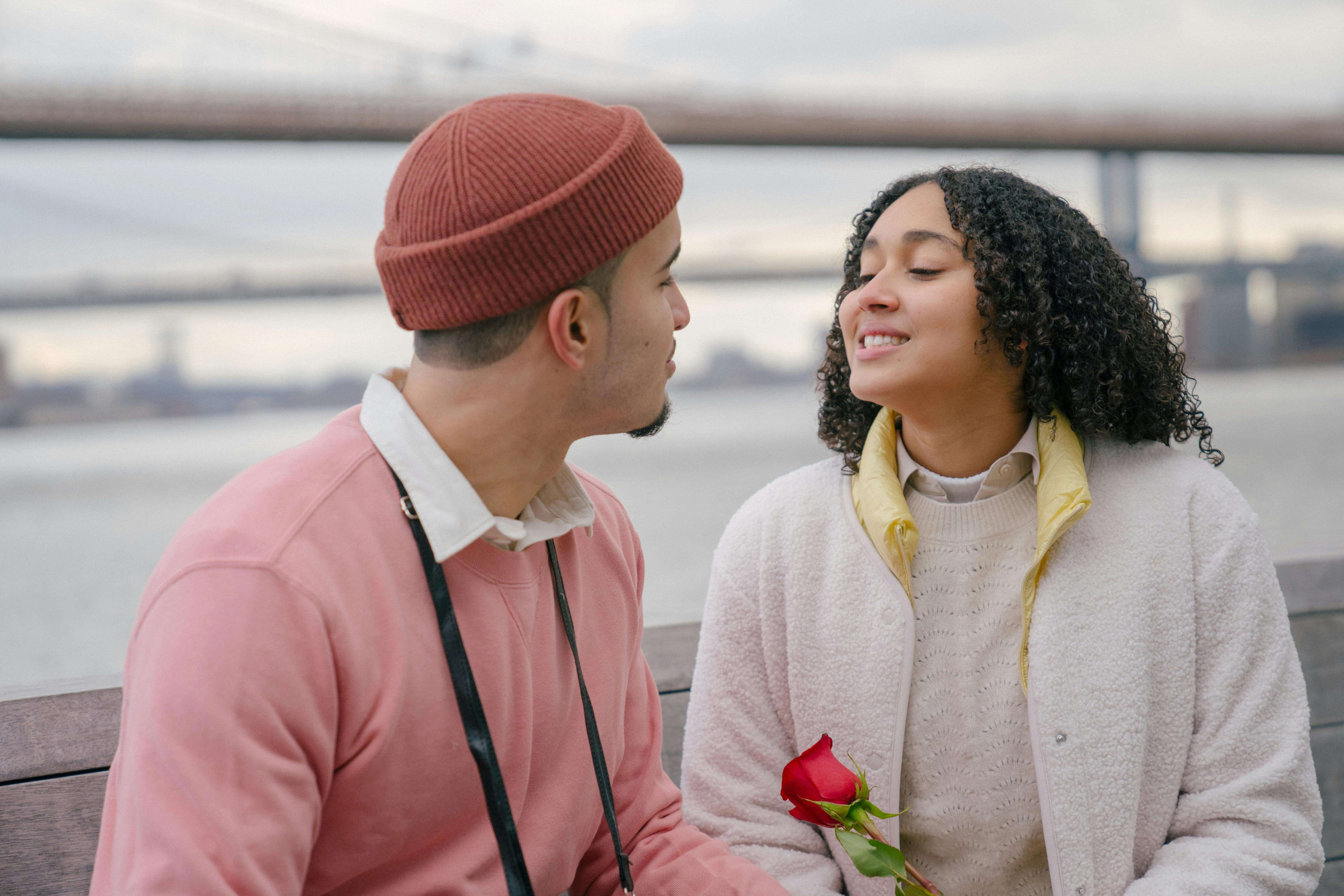Young couple enjoying a romantic moment by the waterfront, holding a red rose.